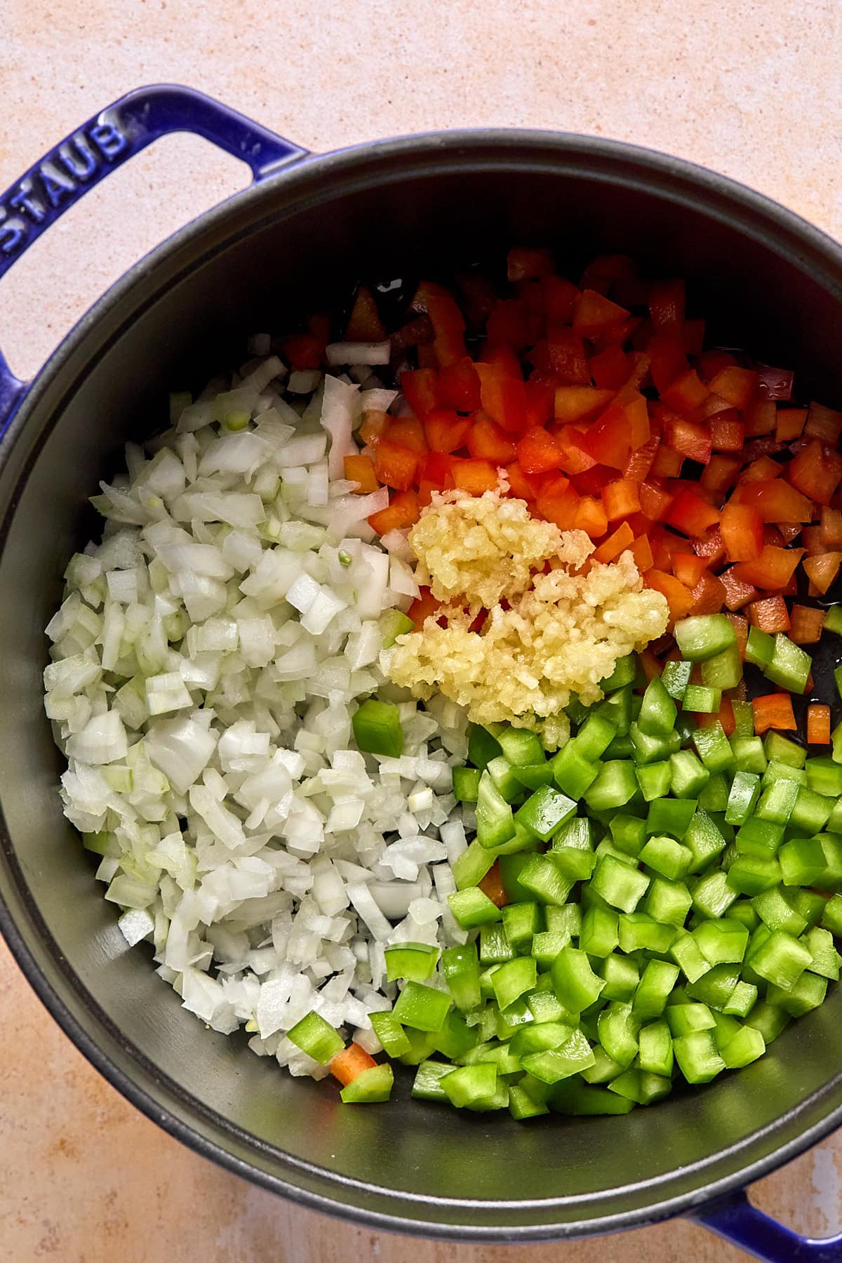 Onions, red and green bell peppers, and garlic sautéing in a large STAUS Dutch oven.