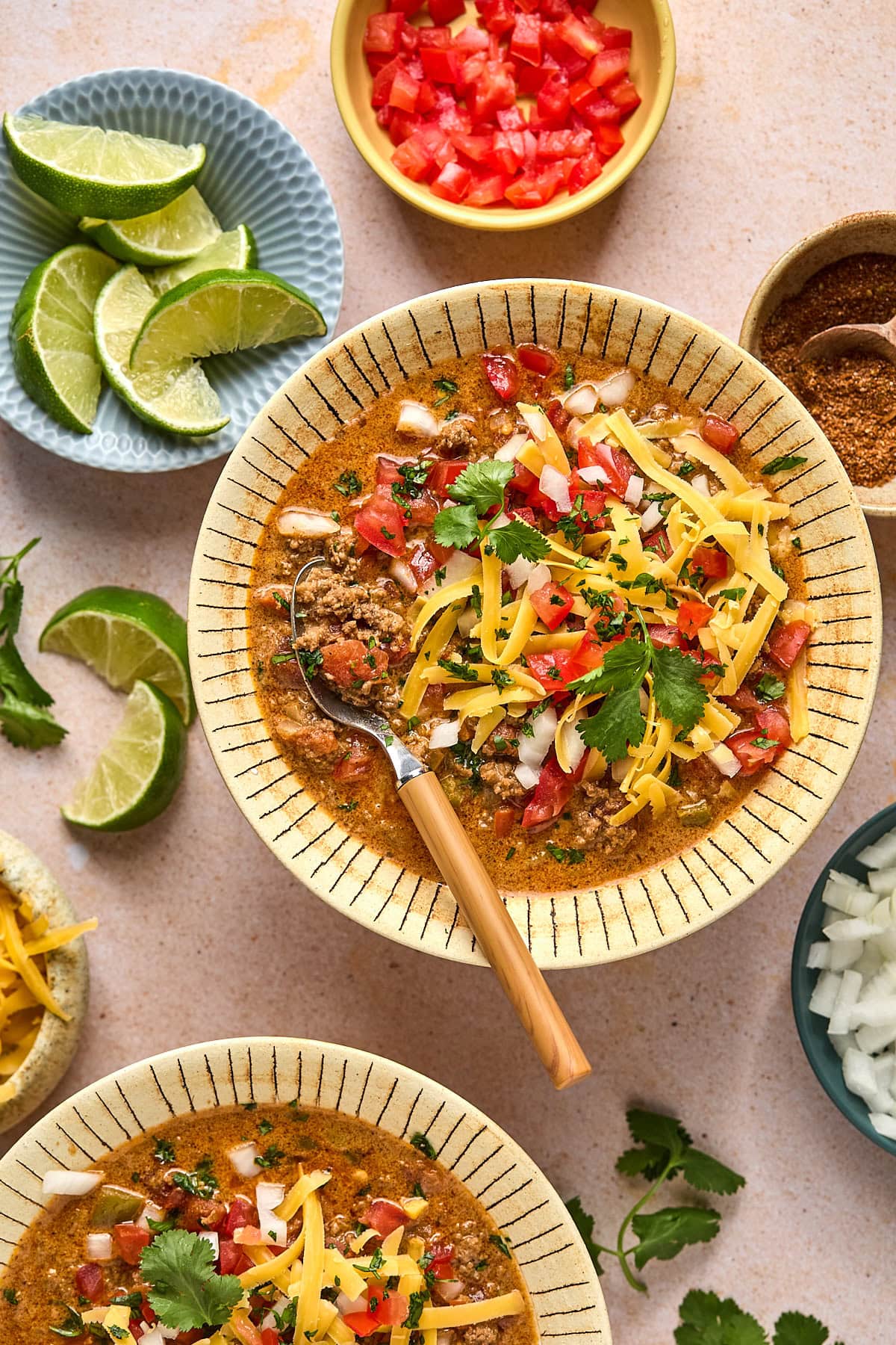 Two bowls of creamy taco soup topped with cilantro, diced onion, and cheese, ready to serve on a pink background.