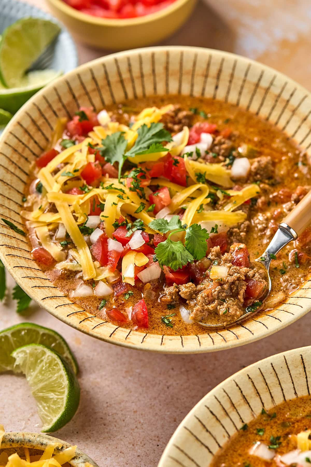 Bowl of creamy taco soup topped with cilantro, shredded cheese, and diced onion, with a spoon ready to eat with an orange-tinted background.