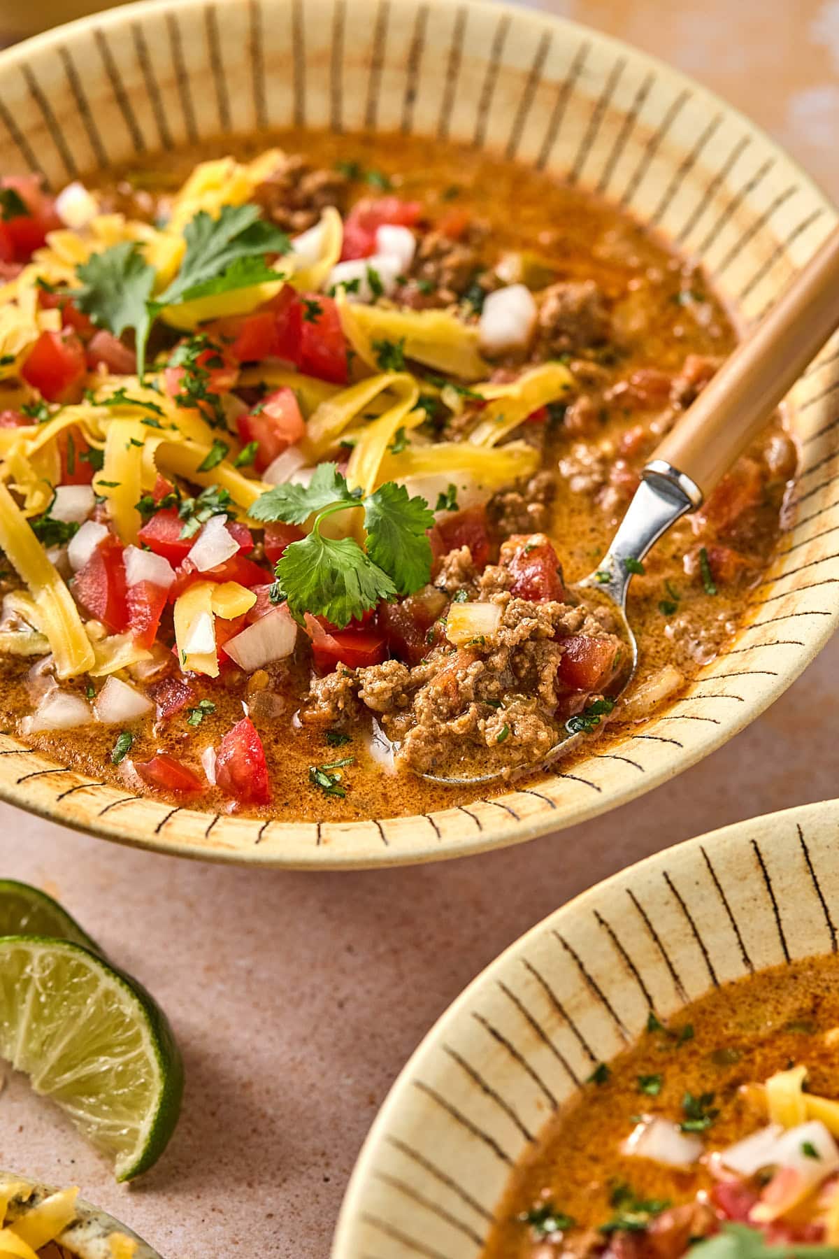 Close-up of creamy taco soup in a bowl topped with cilantro, shredded cheese, and diced onion, with a spoon ready to eat.