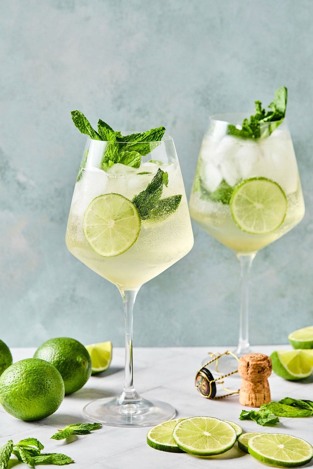 Hugo Spritz recipe in two clear wine glasses garnished with mint and lime, sparkling and chilled on a light background.