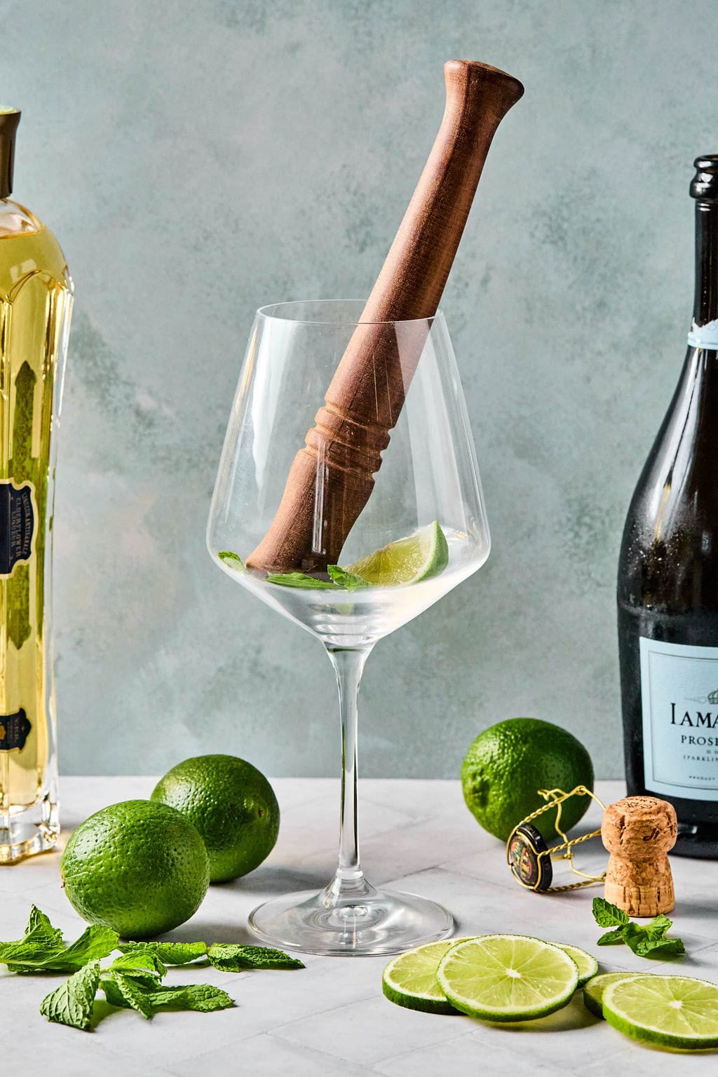 Muddling fresh mint and a lime wedge in a wine glass to start a Hugo Spritz.