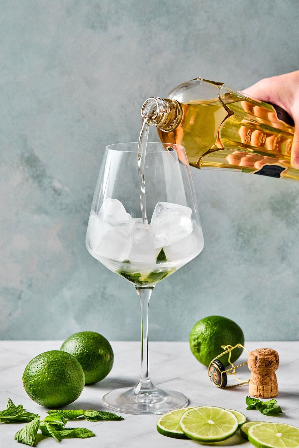 Pouring elderflower liqueur over ice in a wine glass for a Hugo Spritz.