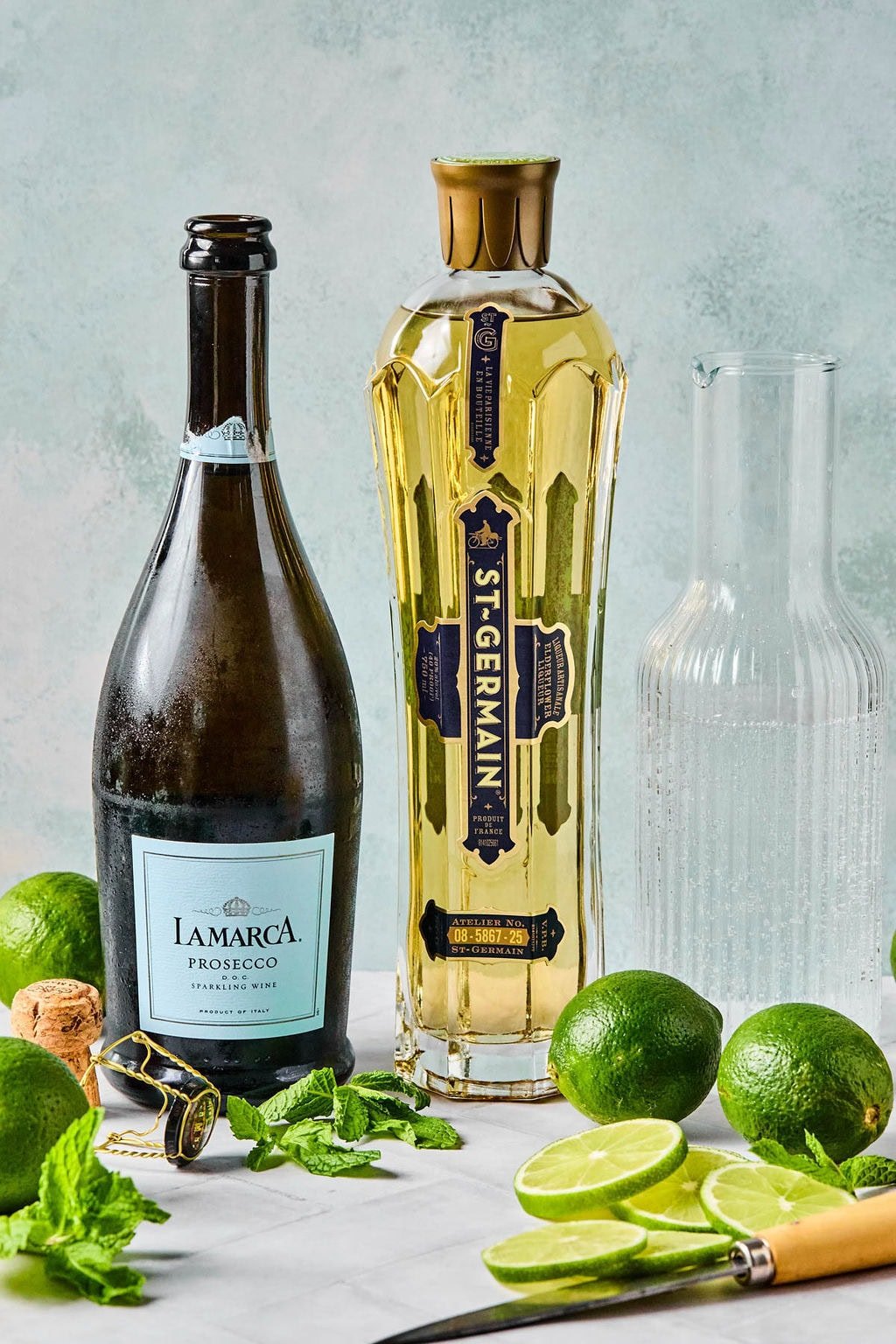 Ingredients for Hugo Spritz including prosecco, elderflower liqueur, sparkling water, fresh mint, and limes.