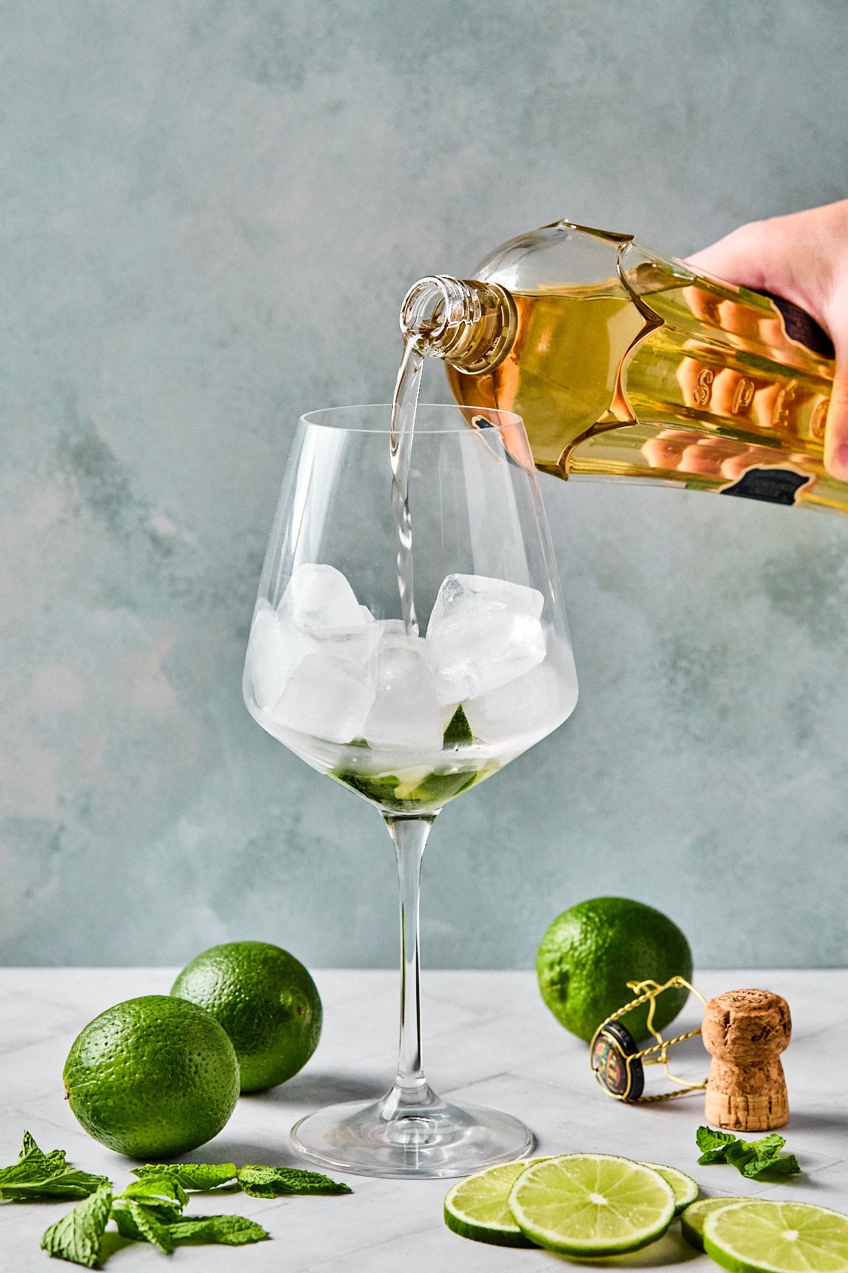 Pouring elderflower liqueur over ice in a wine glass for a Hugo Spritz.