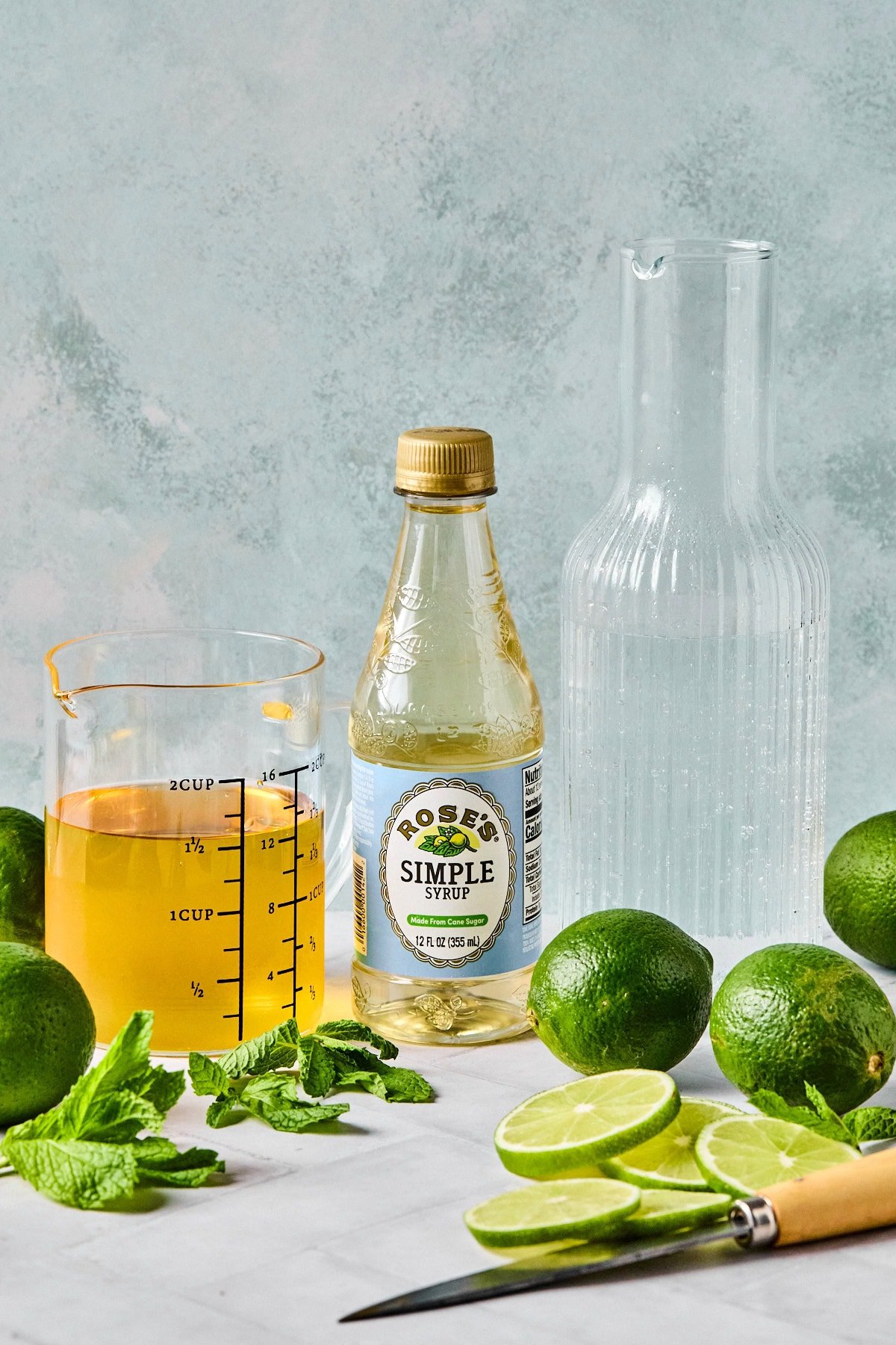 Mocktail Hugo Spritz ingredients including sparkling water, white grape juice, elderflower syrup, fresh mint, and limes.