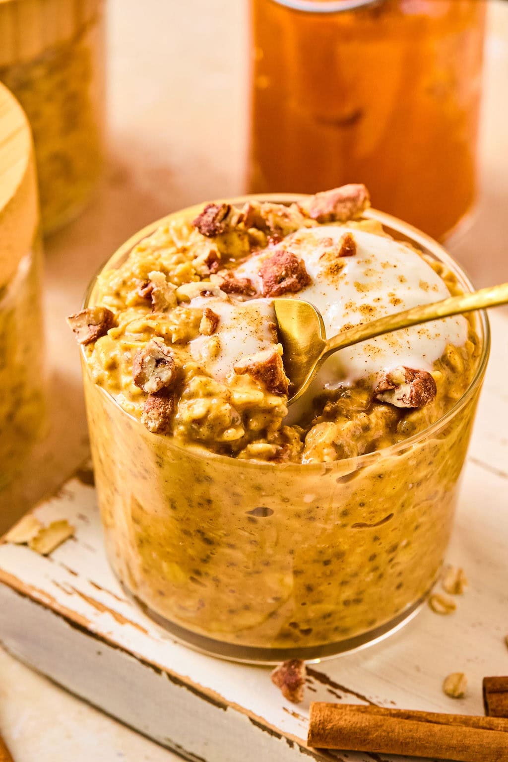 Pumpkin pie overnight oats in a glass jar topped with chopped honey roasted pecans and maple-sweetened greek yogurt.