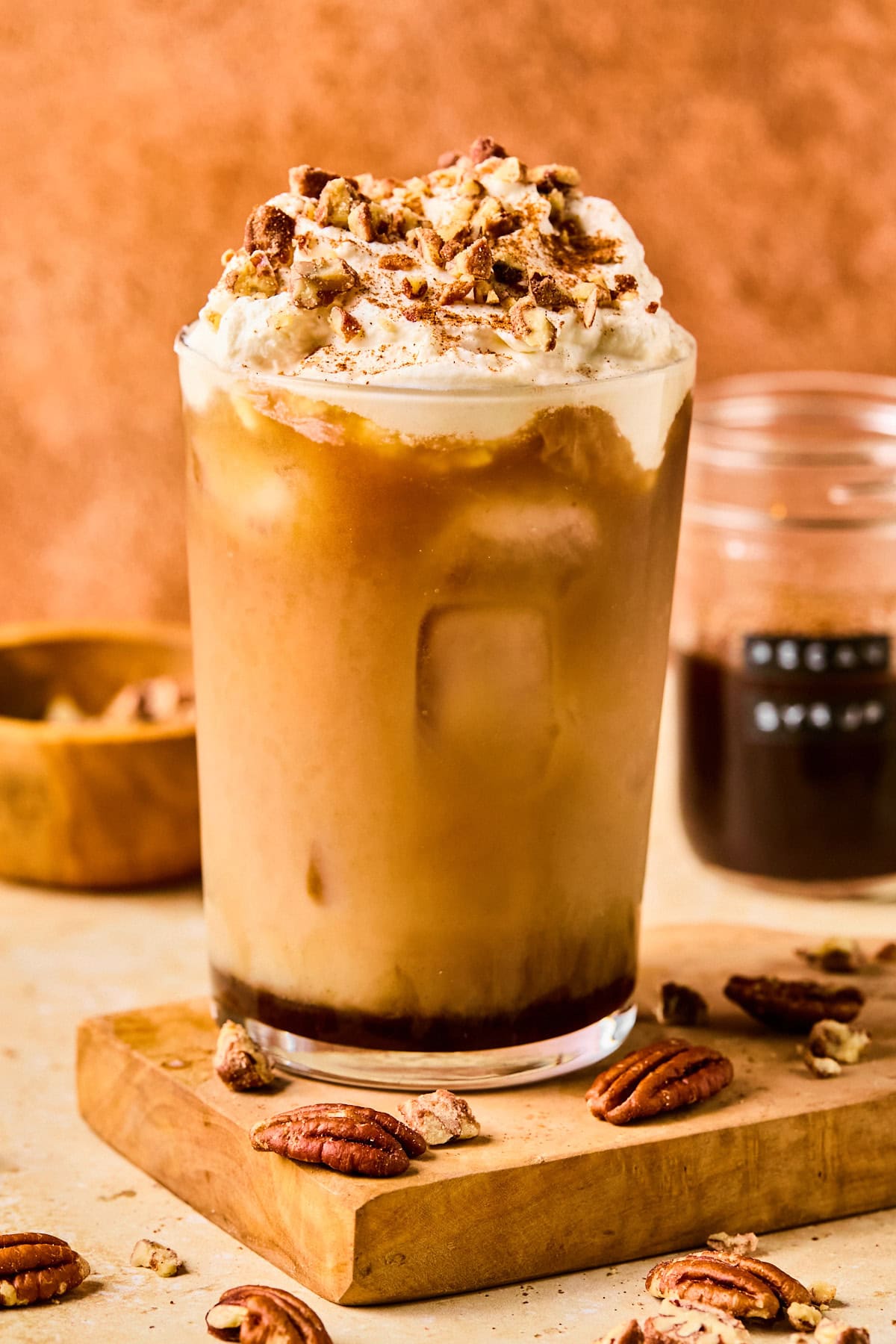 Iced pecan crunch oatmilk latte in a tall glass topped with whipped oat cream, cinnamon, and chopped pecans.