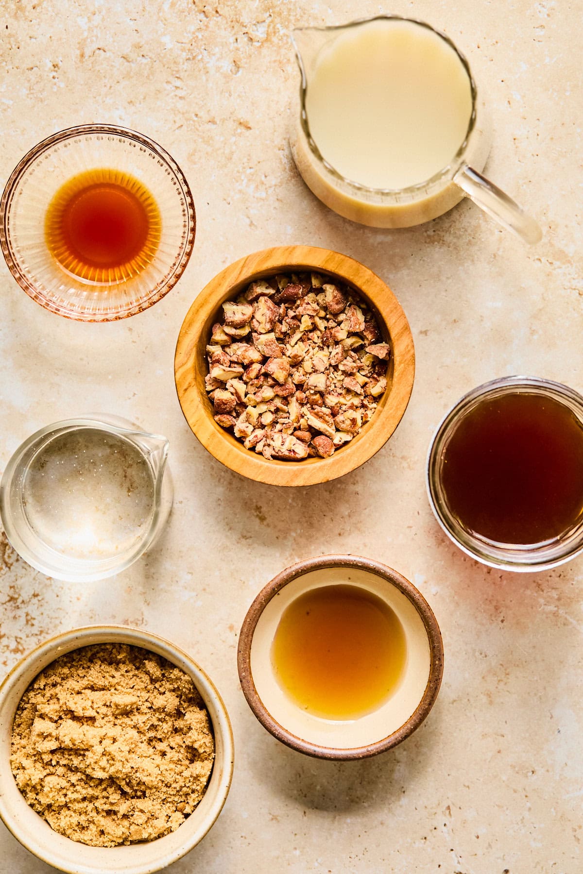 Ingredients for a pecan crunch oatmilk latte including chopped honey-roasted pecans, espresso, barista-style oat milk, pecan syrup, maple syrup, and brown sugar.