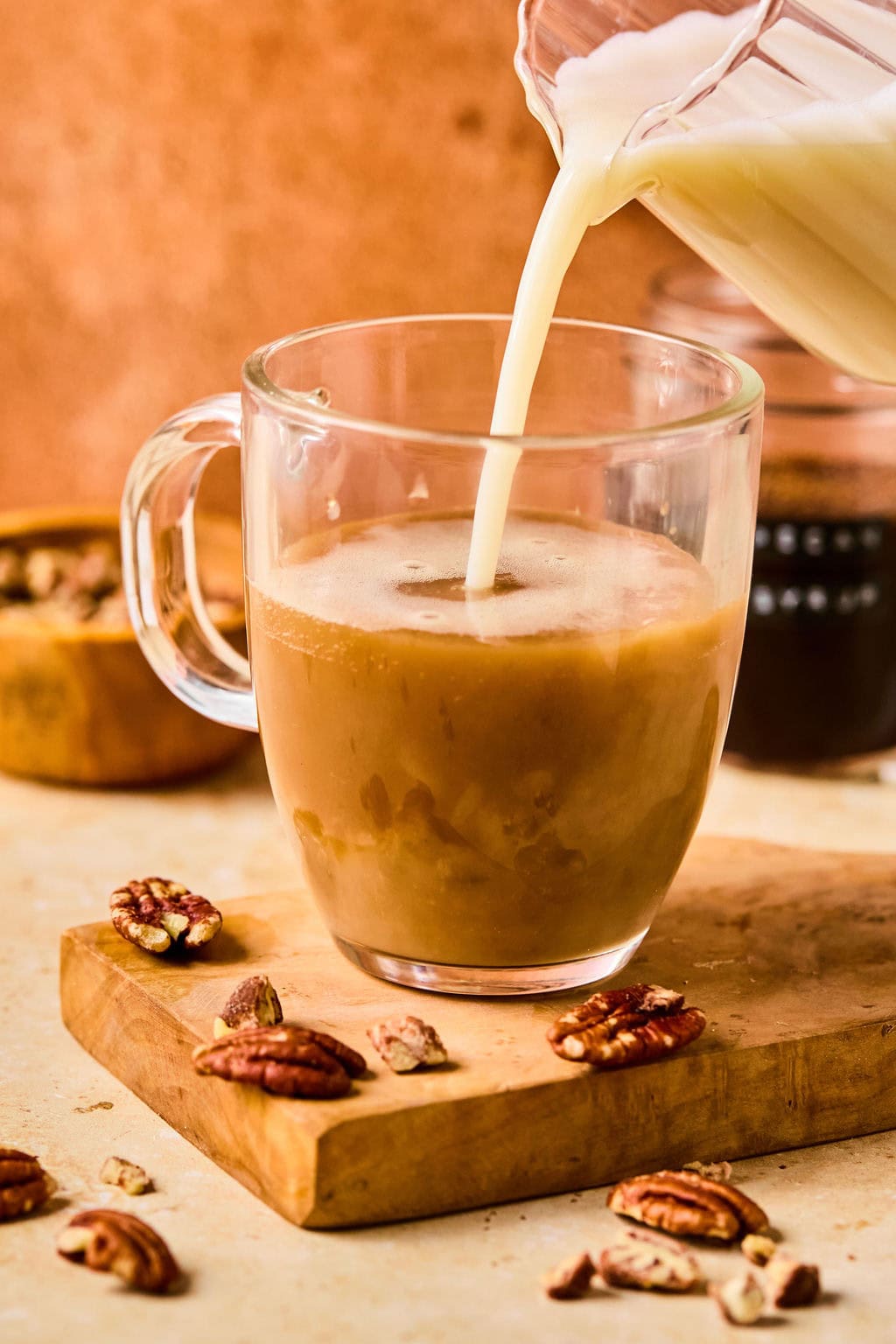 Steaming oat milk being poured over  pecan syrup and espresso in a glass mug.