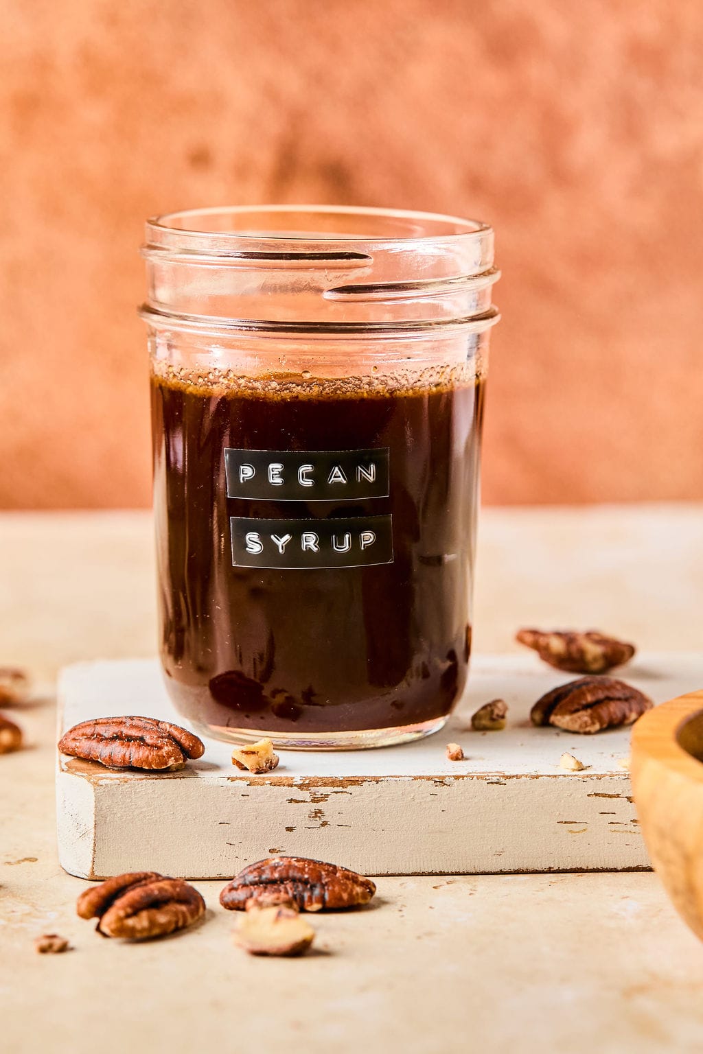 Close-up of homemade pecan syrup in a small glass jar in front of an orange backdrop.