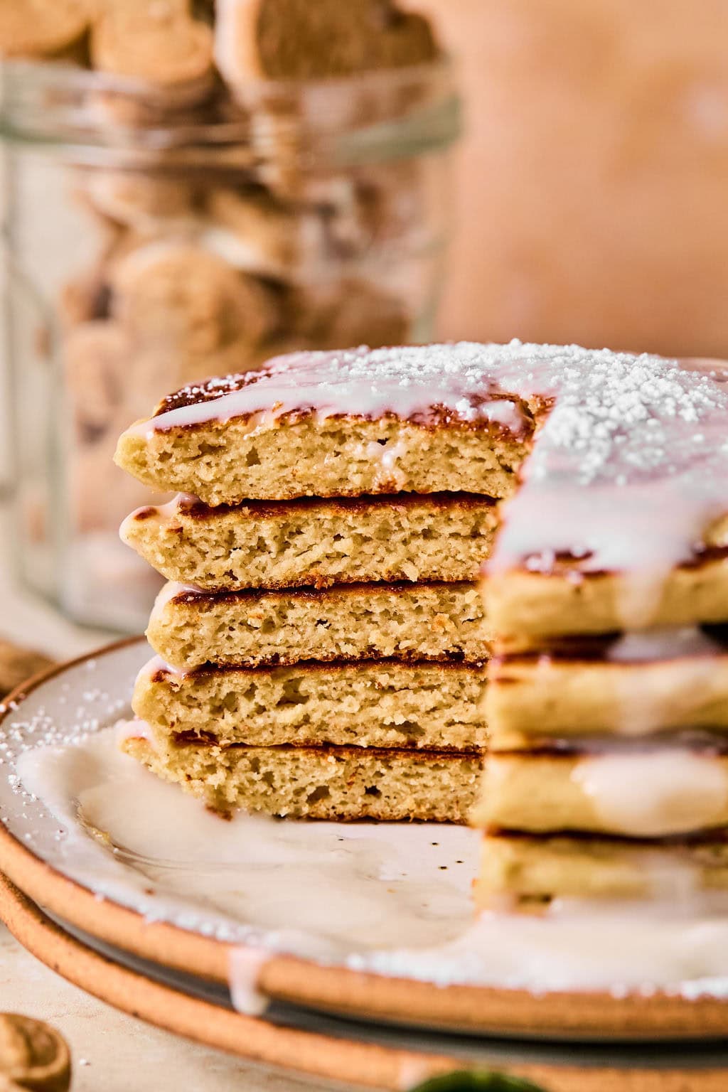 Close-up of a stack of gingerbread pancakes on a plate drizzled with glaze, with a corner piece cut out of each pancake.