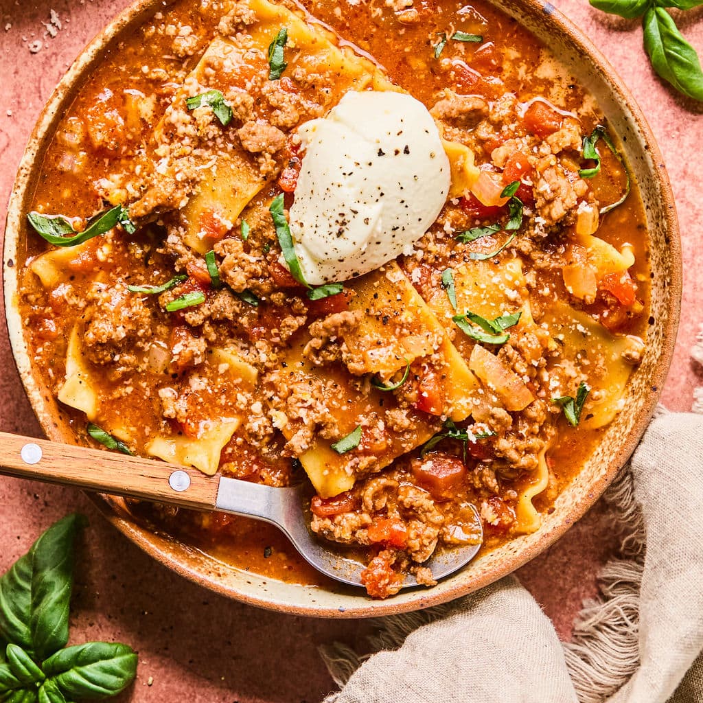 Lasagna soup recipe ladled into a bowl garnished with ricotta cheese and fresh basil.