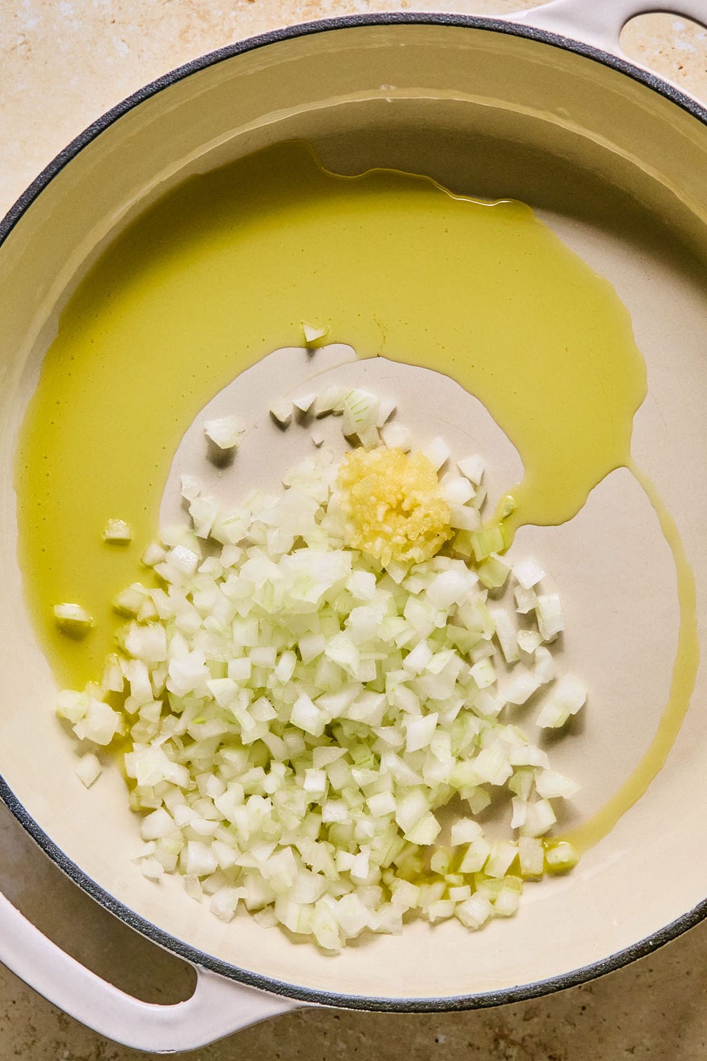 A large skillet with oil, garlic, and chopped onion. 