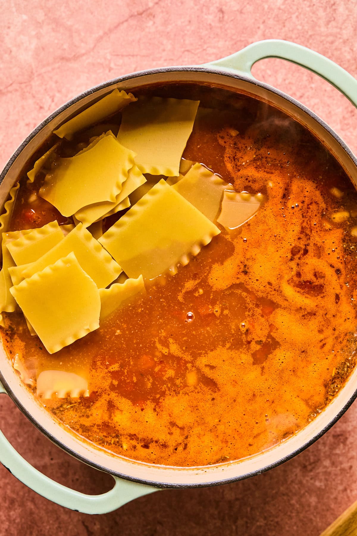 Broken pieces of lasagna noodles being stirred into the soup. 
