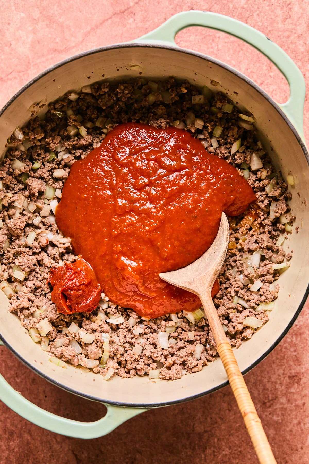 Marinara sauce and tomato paste in a Dutch oven with cooked Italian sausage, ground beef, and onion.