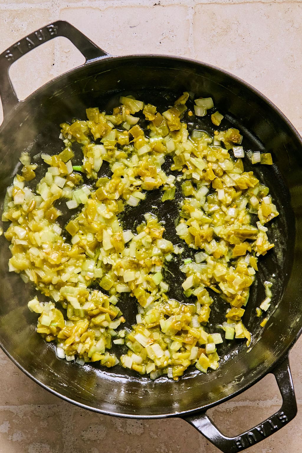 Large skillet with chopped onion, garlic, and green chilies cooked in olive oil.