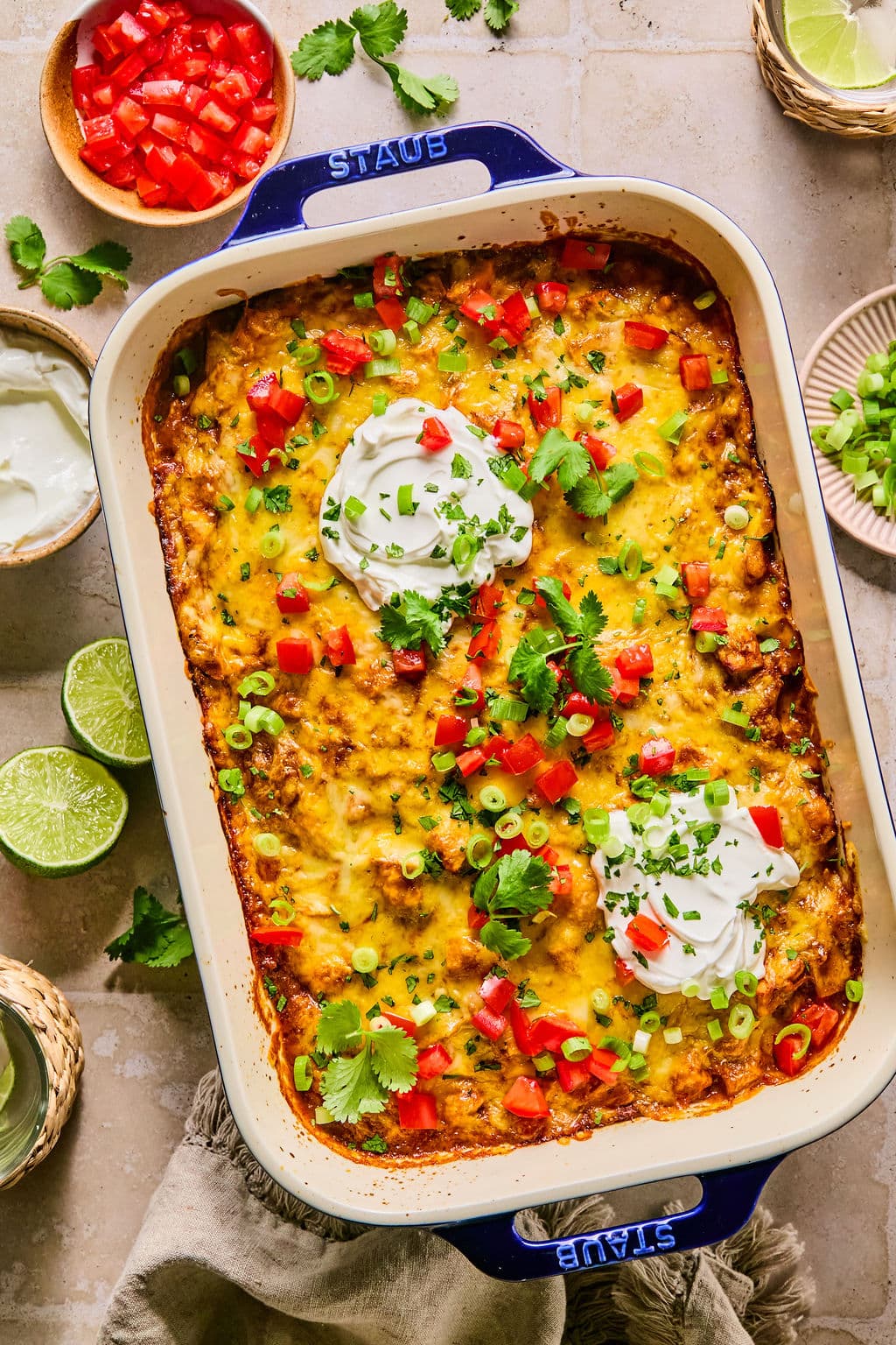 Leftover turkey enchilada casserole in a large baking dish, topped with scoops of Greek yogurt and garnished with diced tomatoes, cilantro, and sliced green onions.