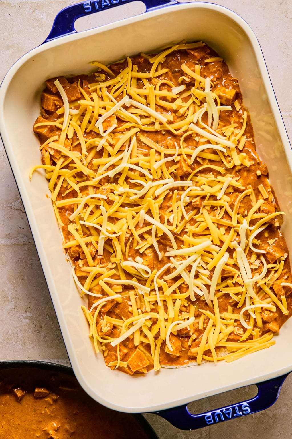 Leftover turkey enchilada casserole layered in a baking dish with a sprinkled of cheddar and Monterey Jack cheese. 