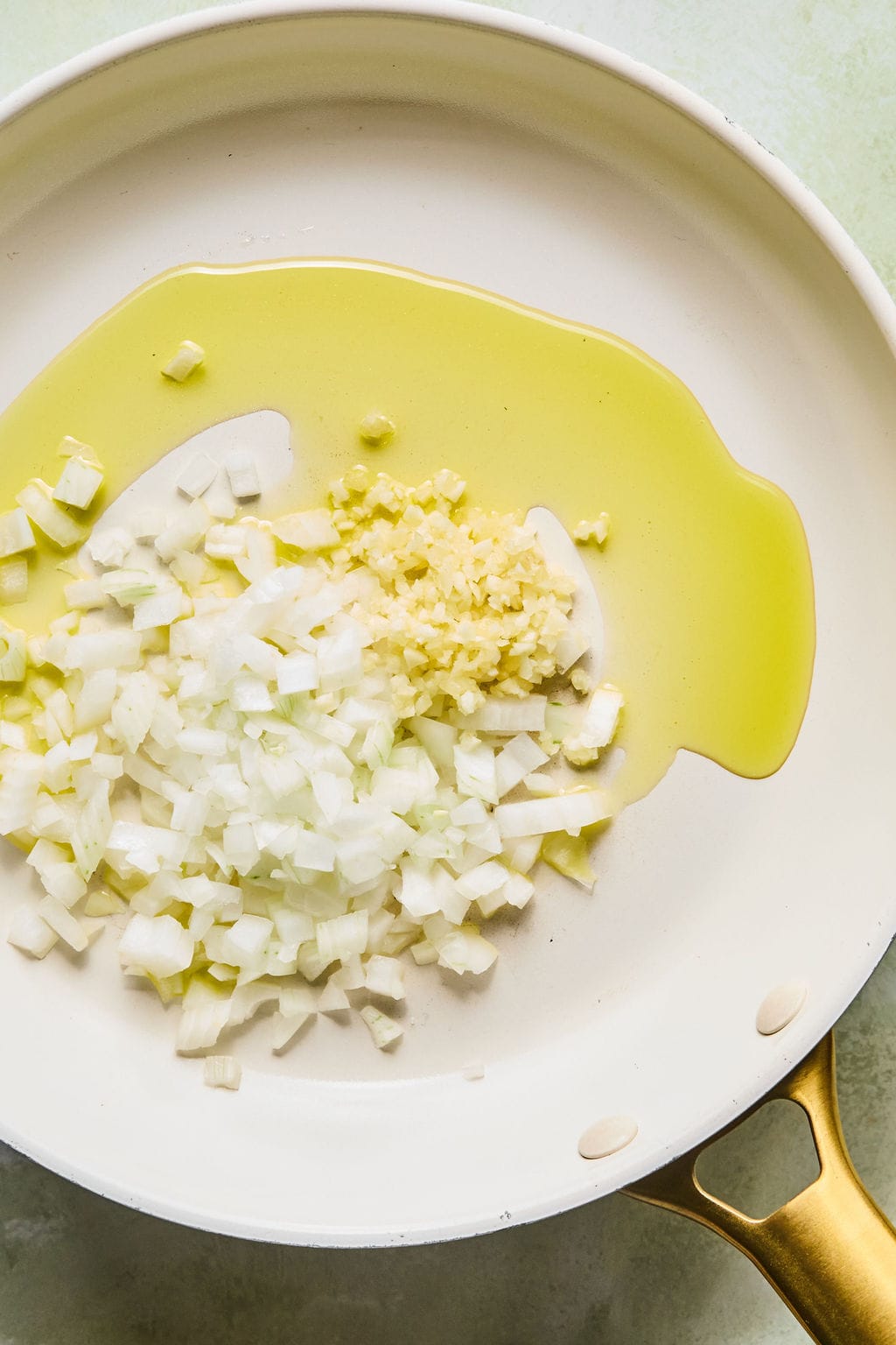 A skillet with olive oil, chopped onion, and garlic.