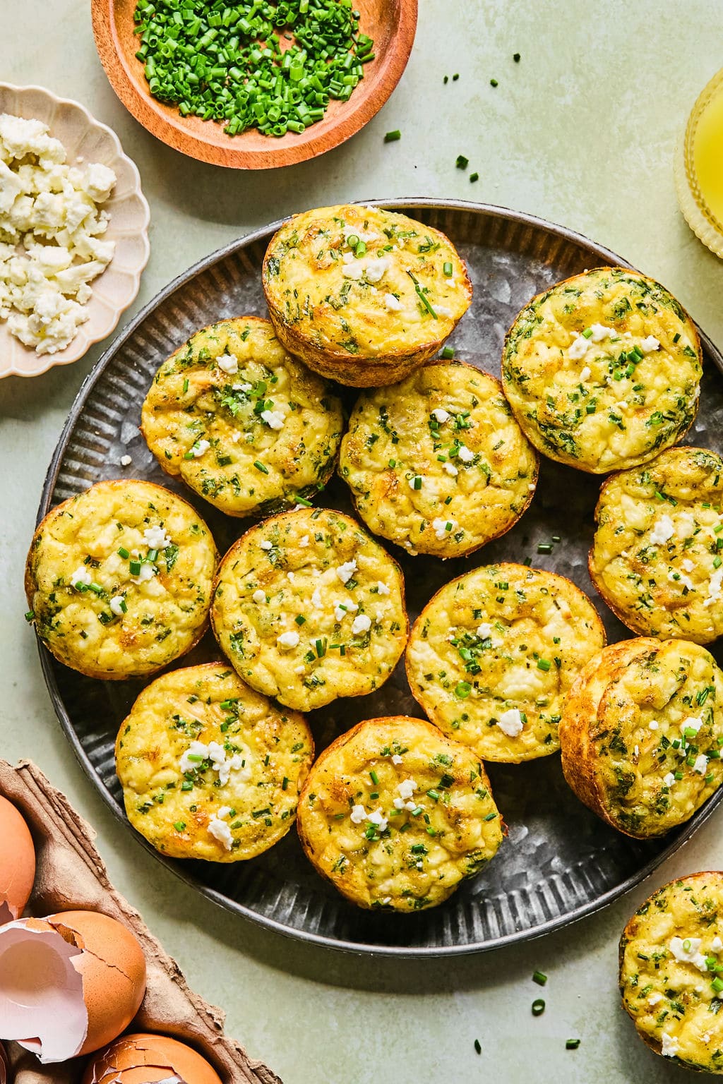 Thanksgiving frittata breakfast muffins on a dark colored serving tray topped with extra feta cheese and chives.
