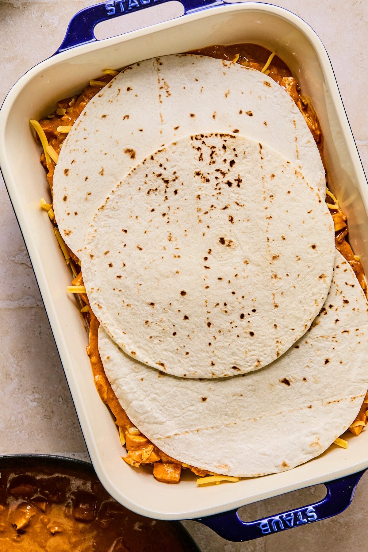 Leftover turkey enchilada casserole layered in a baking dish with 3 overlapping tortillas on top.