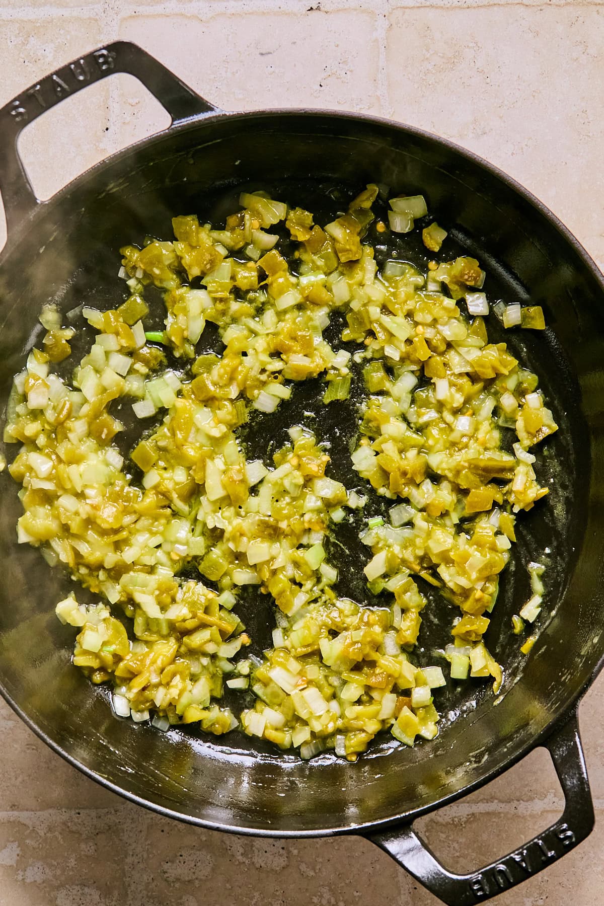 Large skillet with chopped onion, garlic, and green chilies cooked in olive oil.