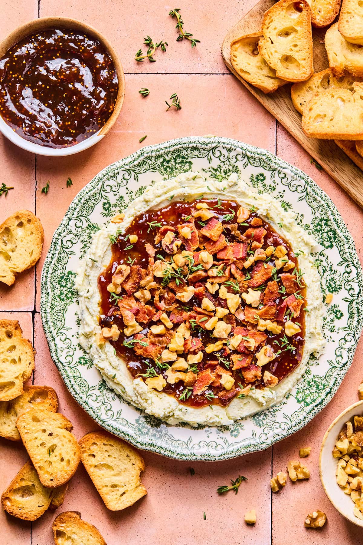 Boursin dip in a shallow serving dish topped with fig jam, cooked bacon pieces, toasted walnuts, and fresh thyme.