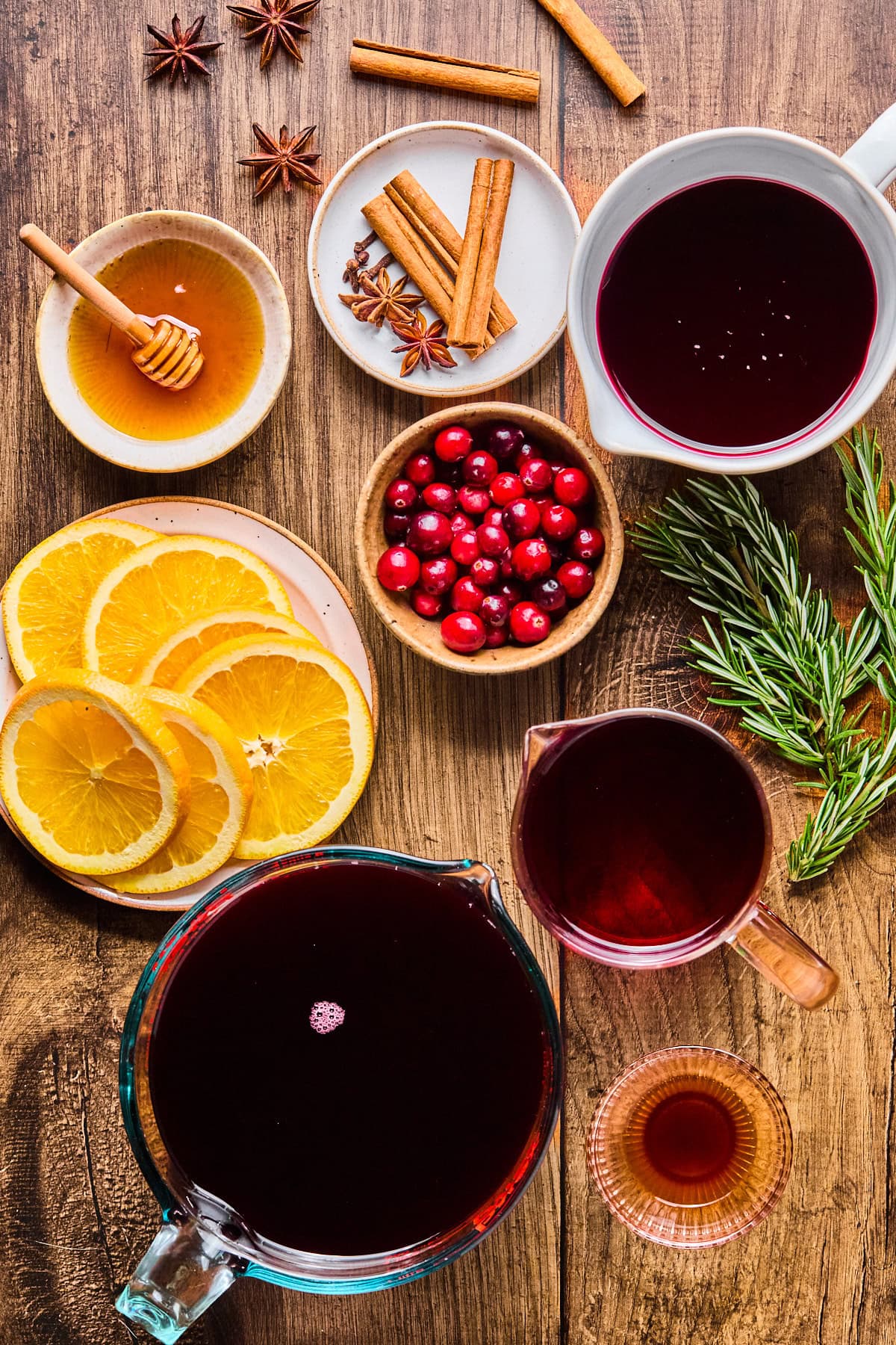 Non alcoholic mulled wine recipe ingredients laid out in nesting bowls and plates on a wooden countertop.