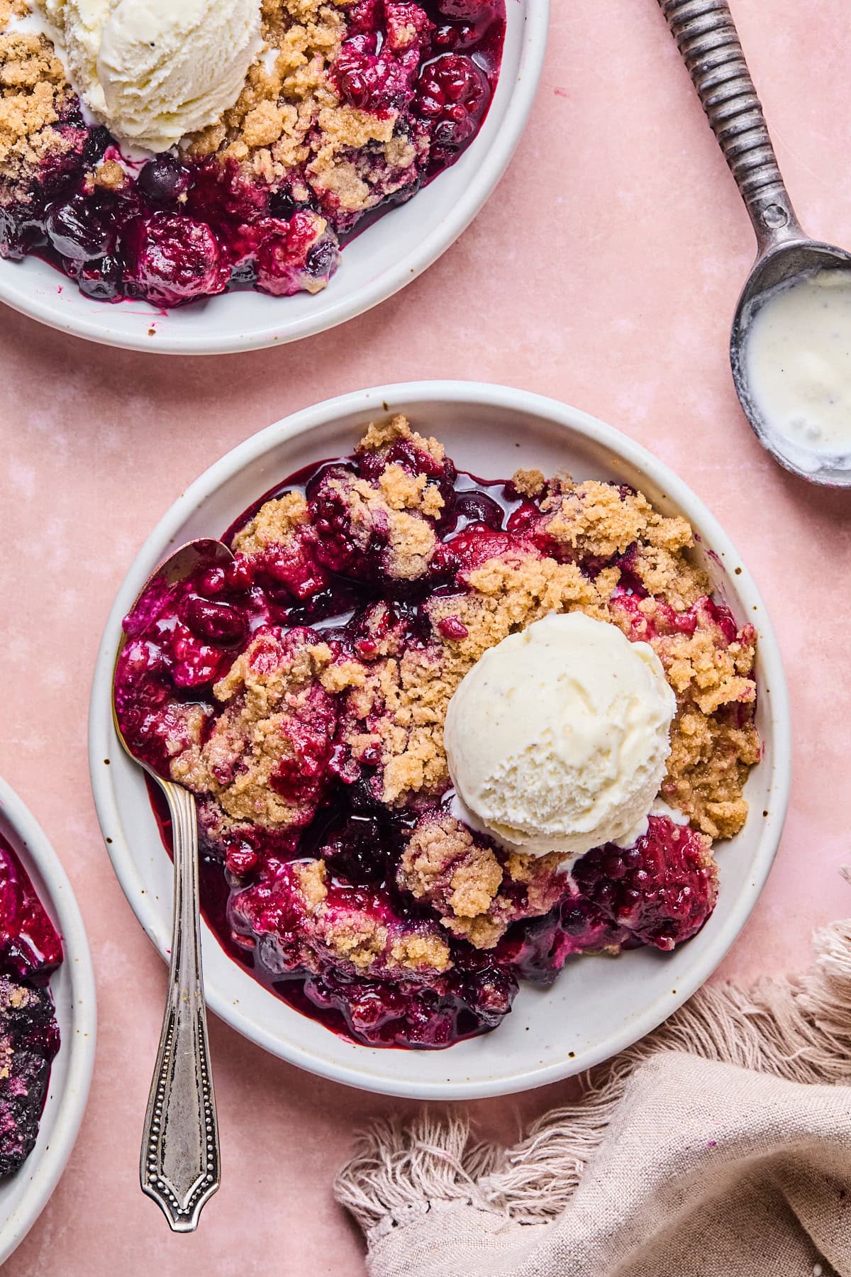 Mixed berry crumble topped with a scoop of vanilla ice cream on a pink backdrop.