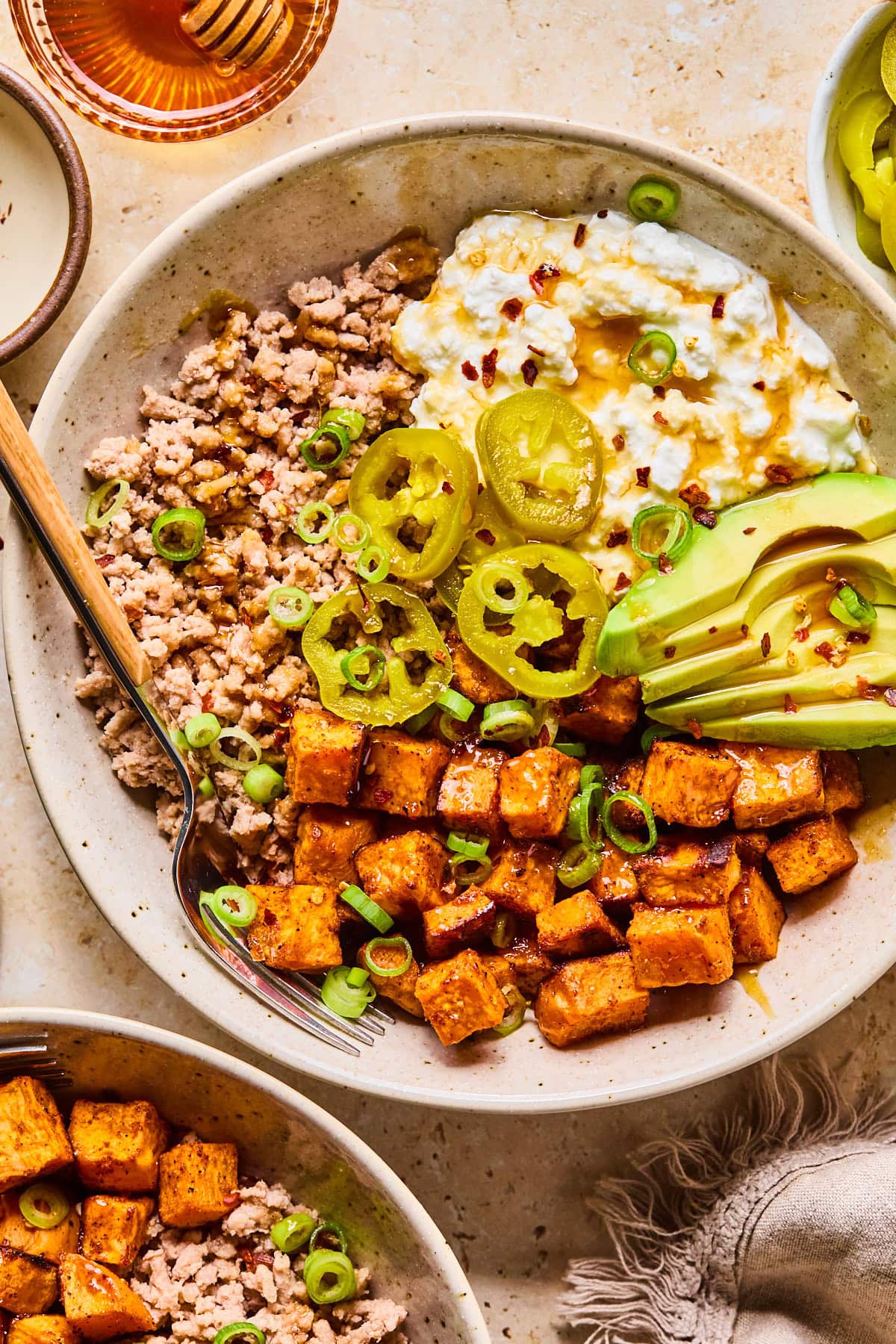 Assembled cheese bowl garnished with green onions, jalapeño slices, red pepper flakes, and a drizzle of hot honey with a fork resting inside.