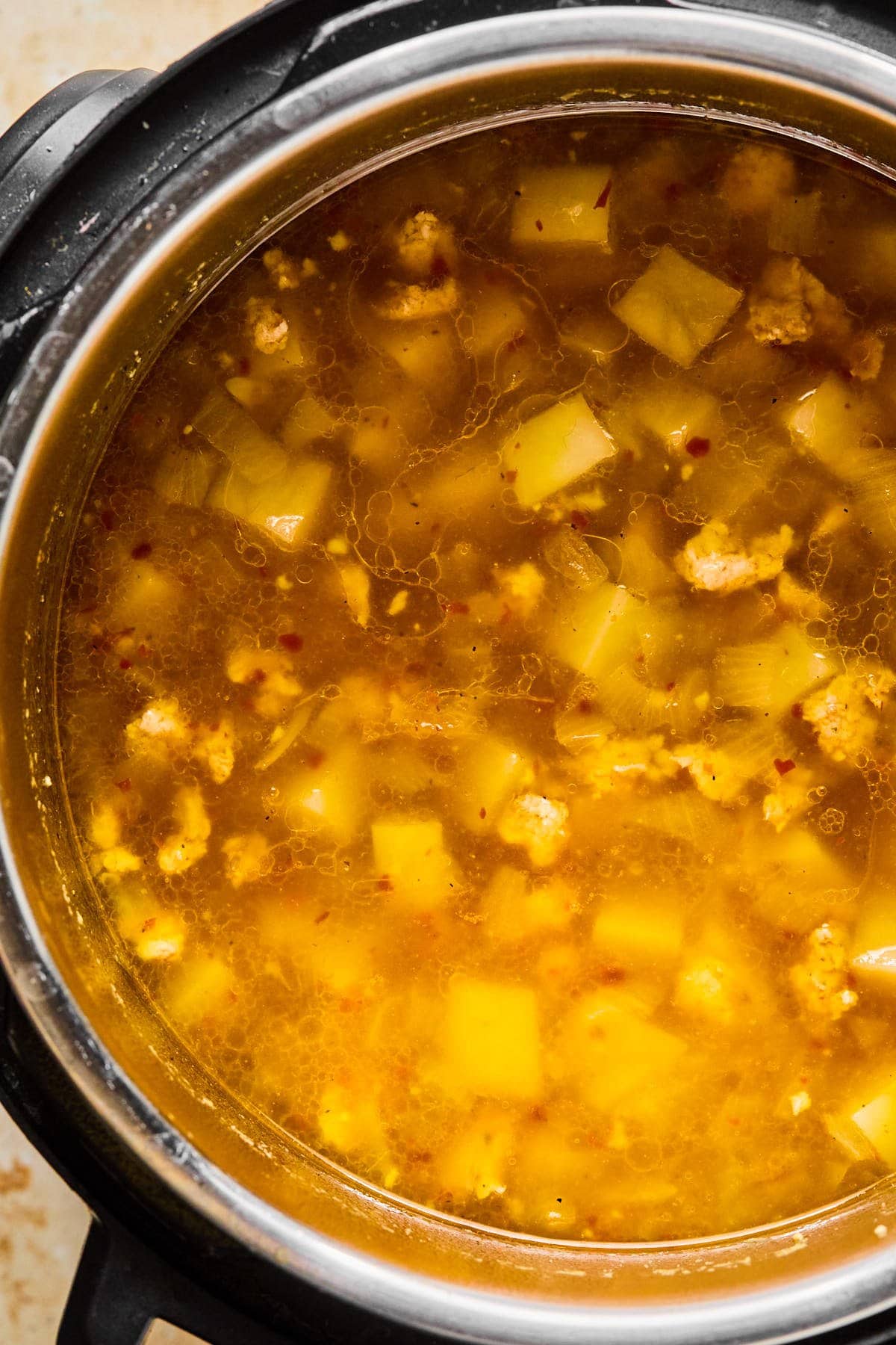 Chicken broth poured into the Instant Pot with cubed potatoes and seasonings added.