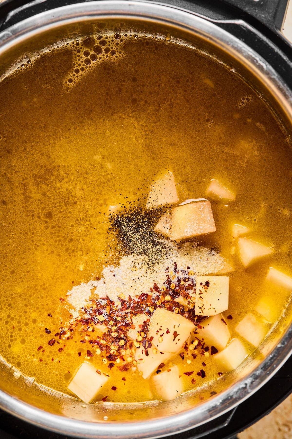 Chicken broth poured into the Instant Pot with cubed potatoes and seasonings added.