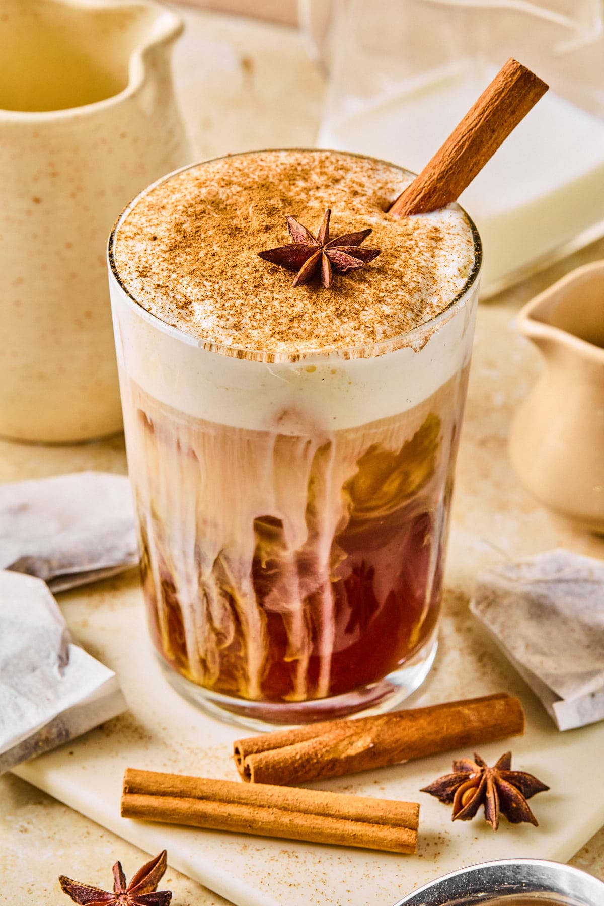 Iced dirty chai latte in a clear glass garnished with ground cinnamon, topped with star anise, and served with a cinnamon stick.