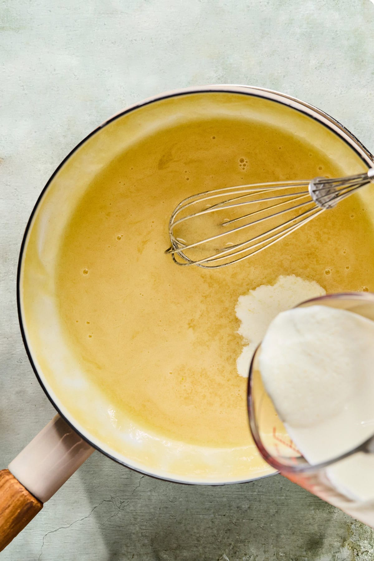 Butter and flour whisked in a saucepan to form a roux with chicken broth, while cream is being poured in.