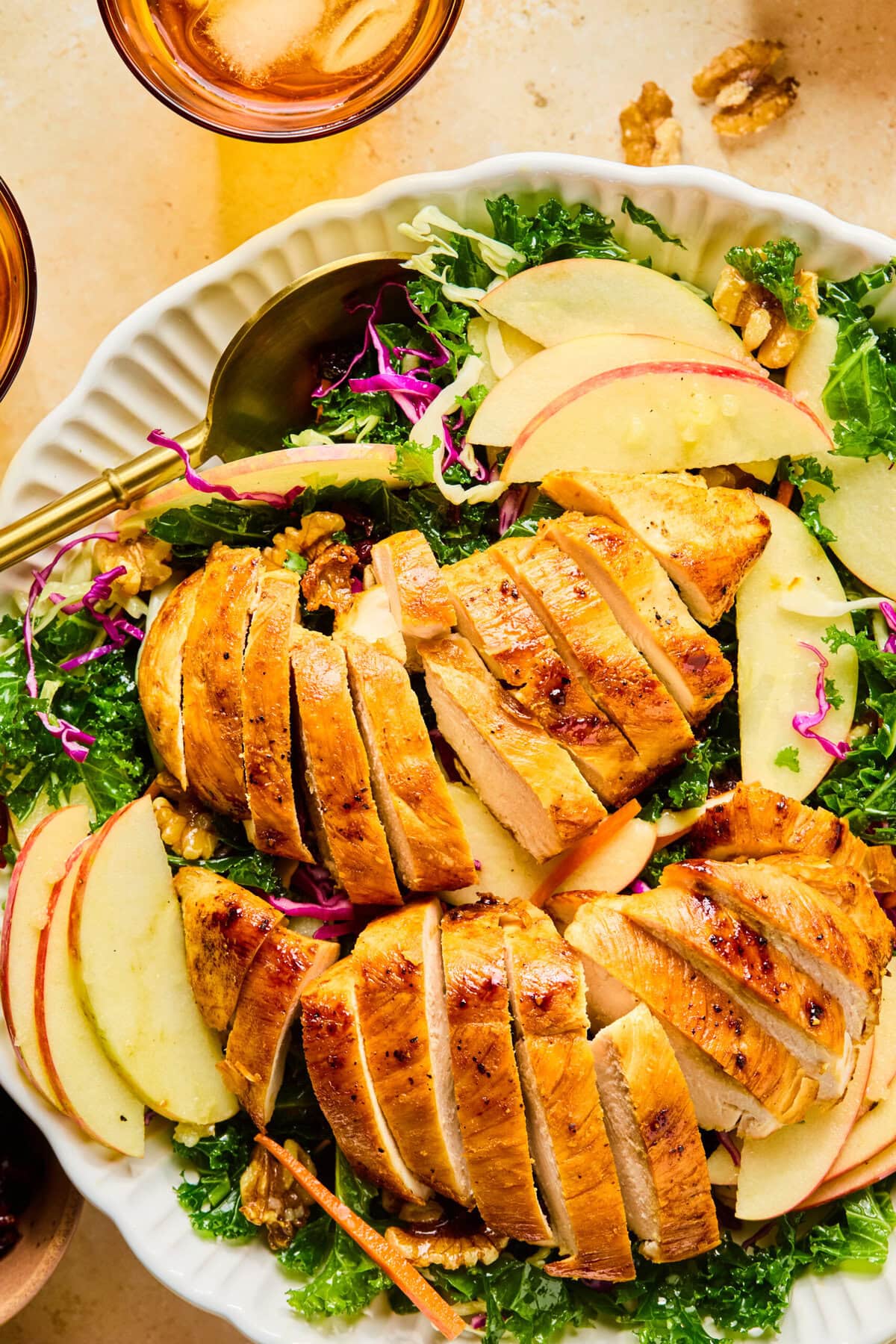 Close-up of winter kale salad showing sliced apples, shredded carrots, grilled chicken, and toasted walnuts.