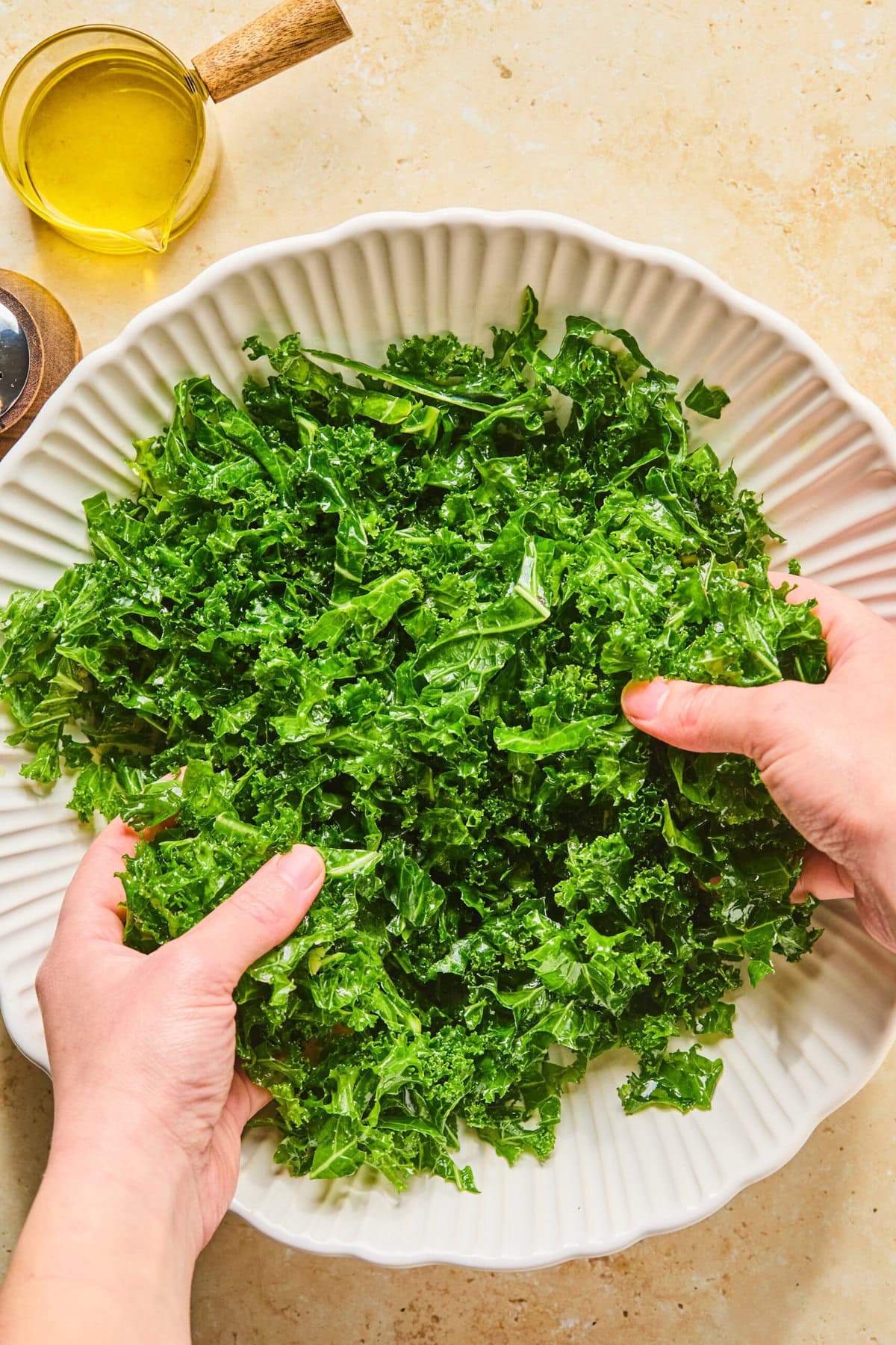 Chopped kale in a large bowl with olive oil and salt being massaged by hand.