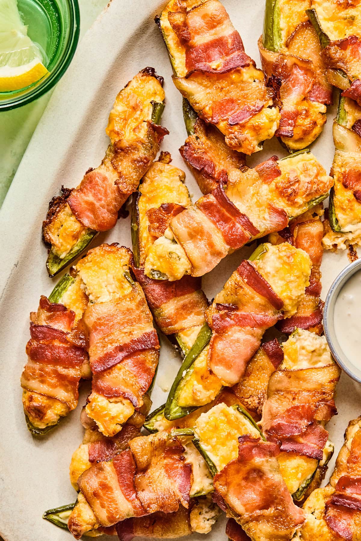 Overhead view of bacon wrapped jalapeno poppers on a white serving tray with a bowl of homemade ranch.
