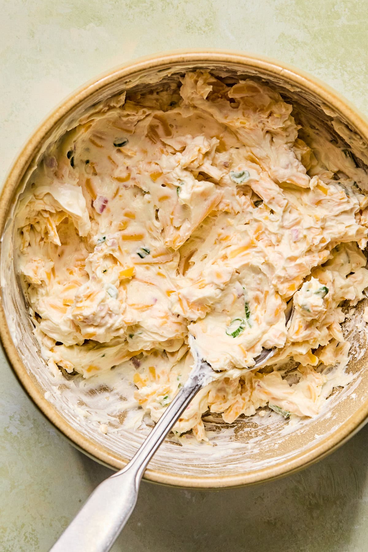 Cream cheese, shredded cheddar, garlic powder, onion powder, shallots, and green onions mixed together in a bowl until smooth and creamy.