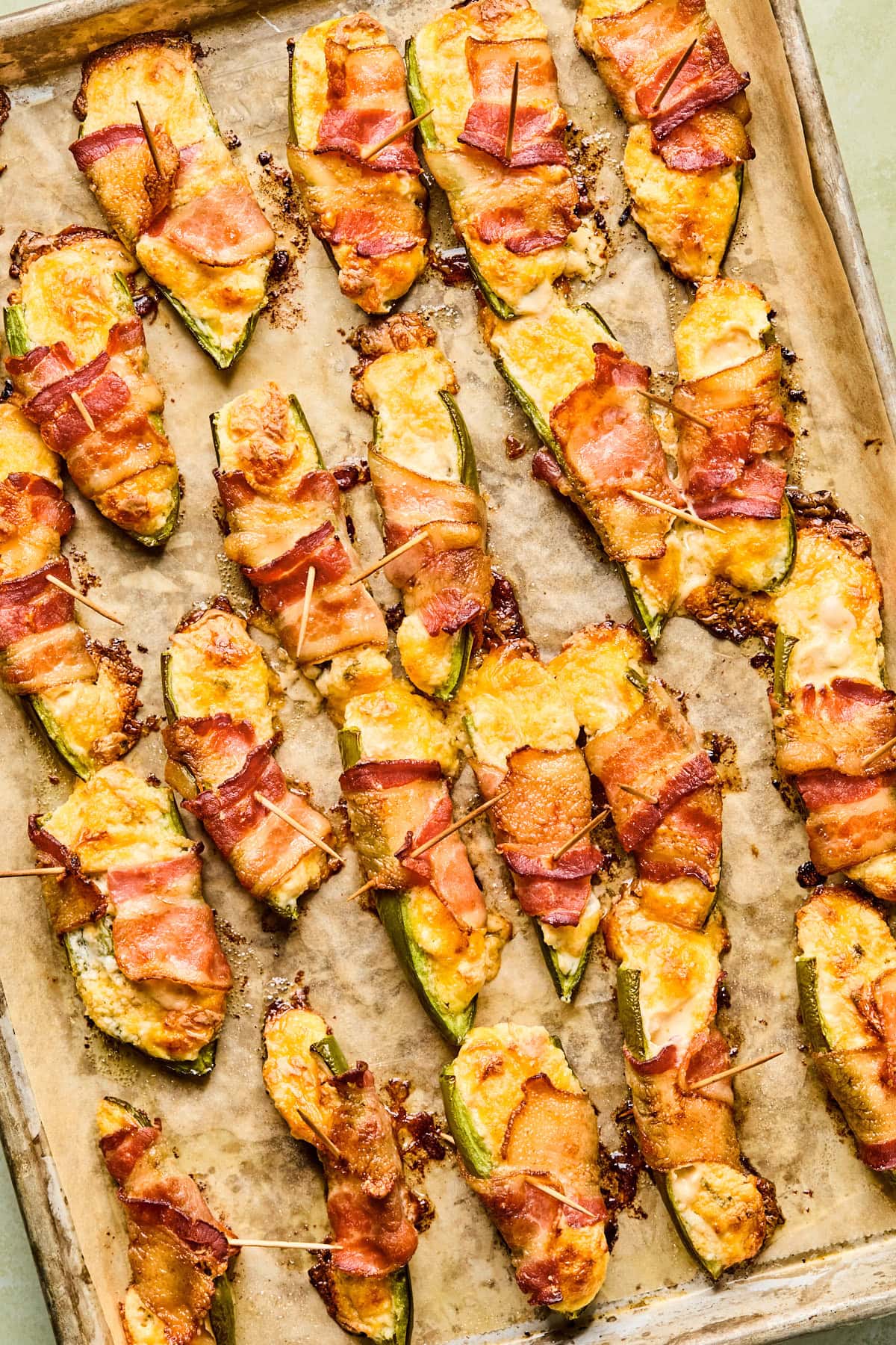 Bacon wrapped jalapeno poppers fresh from the oven cooling on the baking sheet with toothpicks still in them.