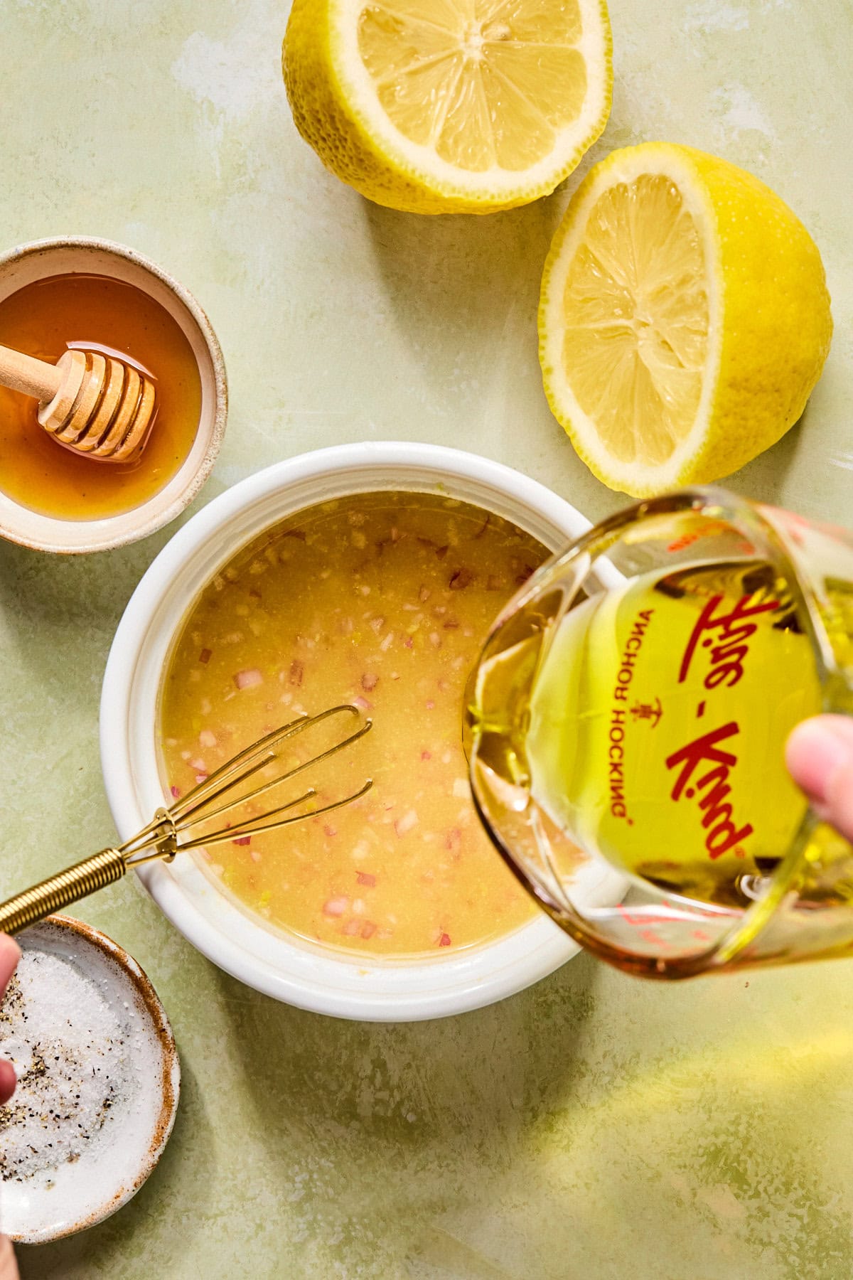 Whisking lemon vinaigrette with Dijon mustard, lemon juice, shallot, vinegar, honey, and olive oil in a small bowl.