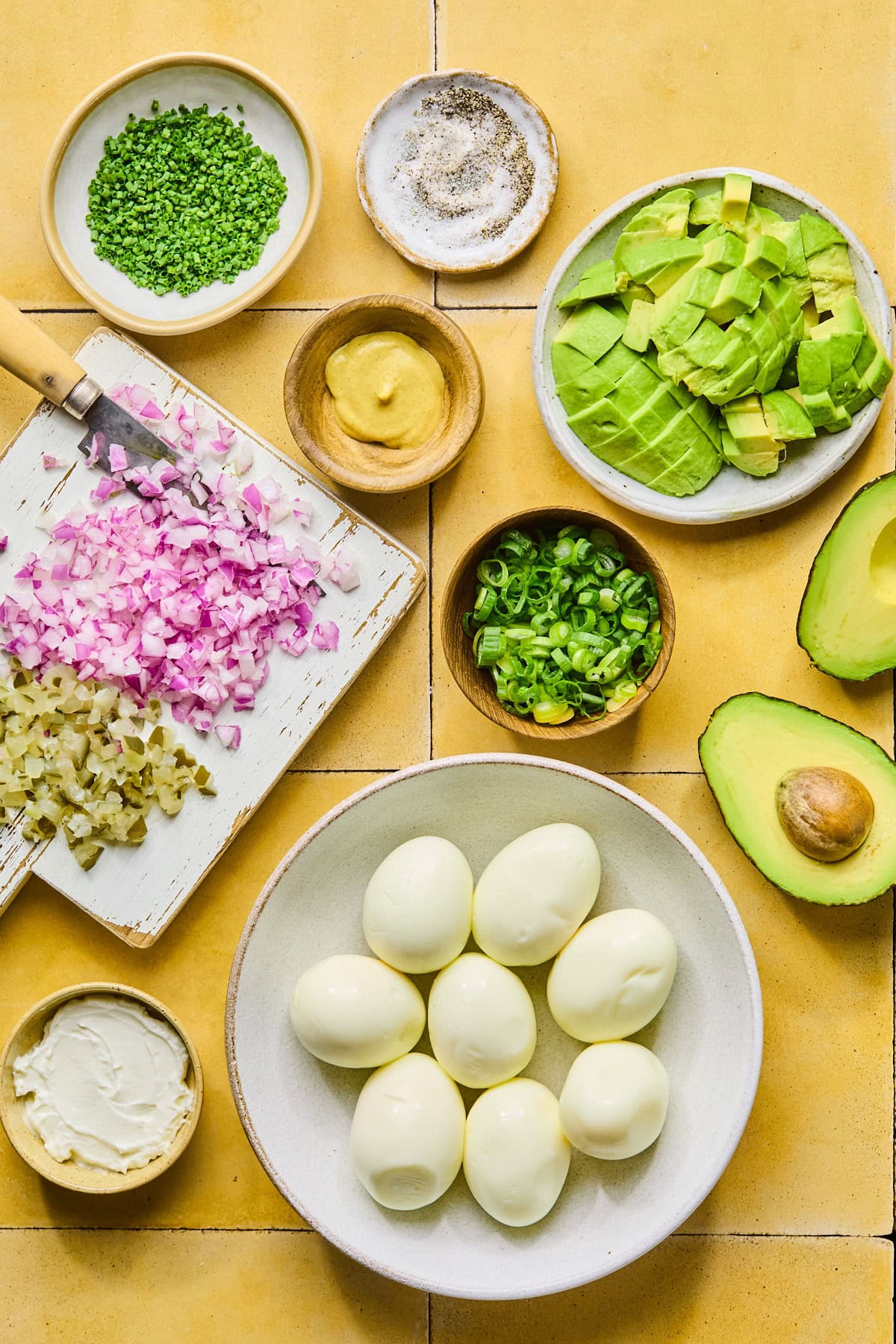 Ingredients for avocado egg salad laid out on a countertop in nesting bowls.