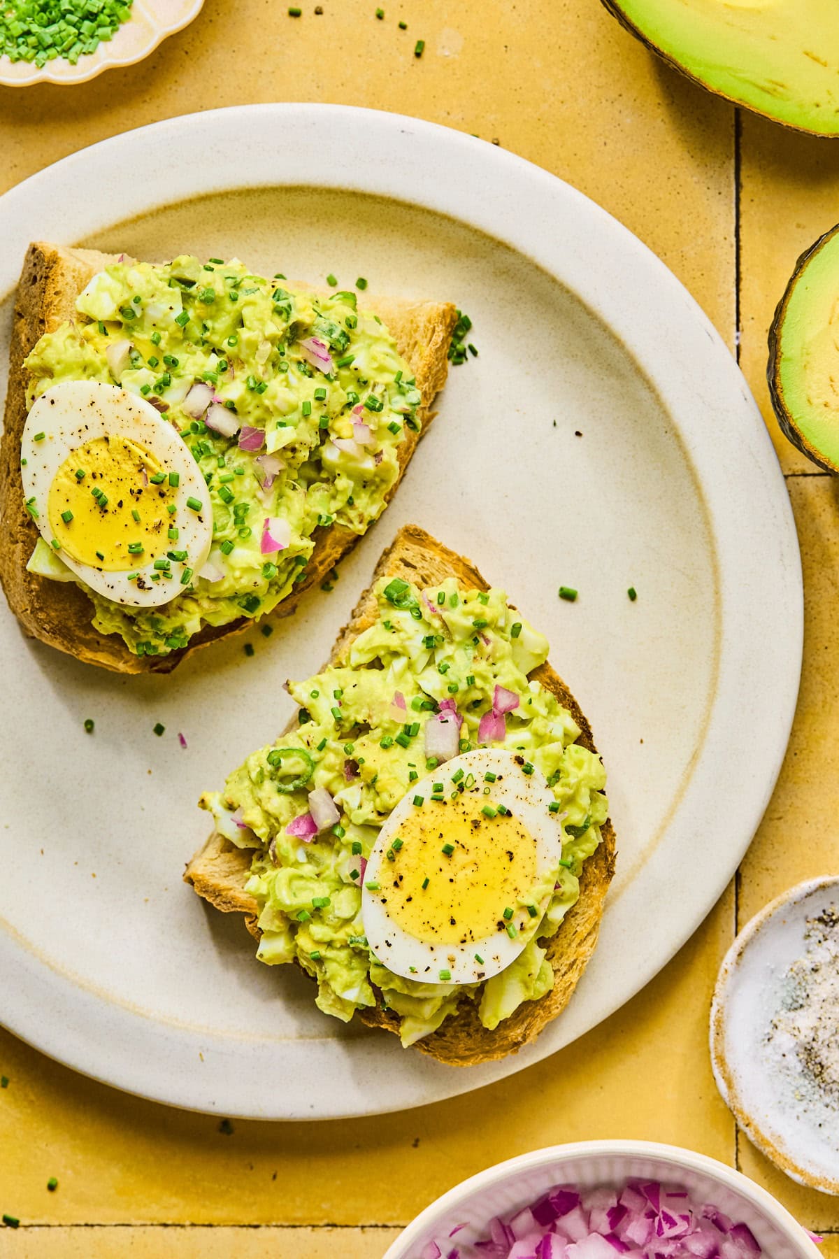 Two slices of toast topped with avocado egg salad served on a plate.