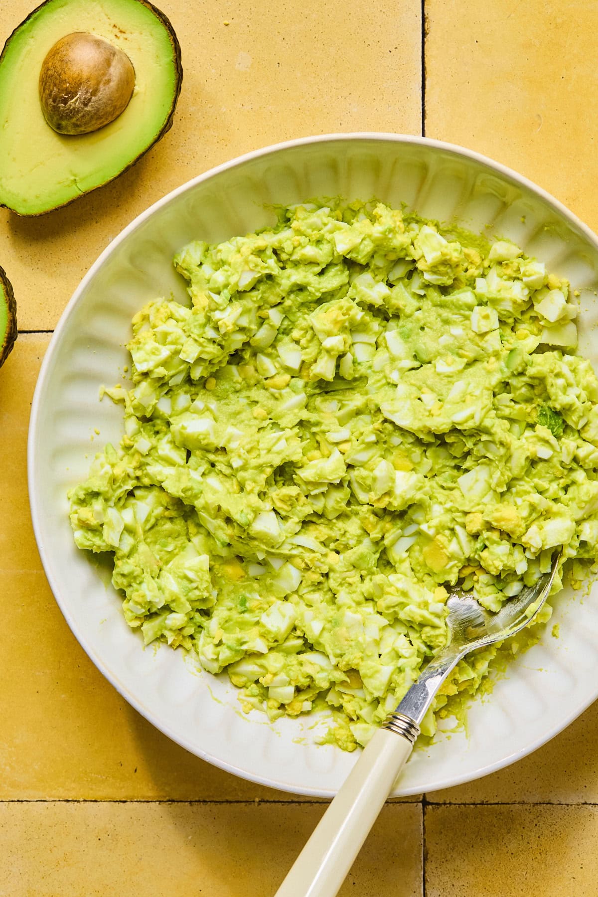 Mashed avocado added to chopped eggs in a bowl and gently mixed together.