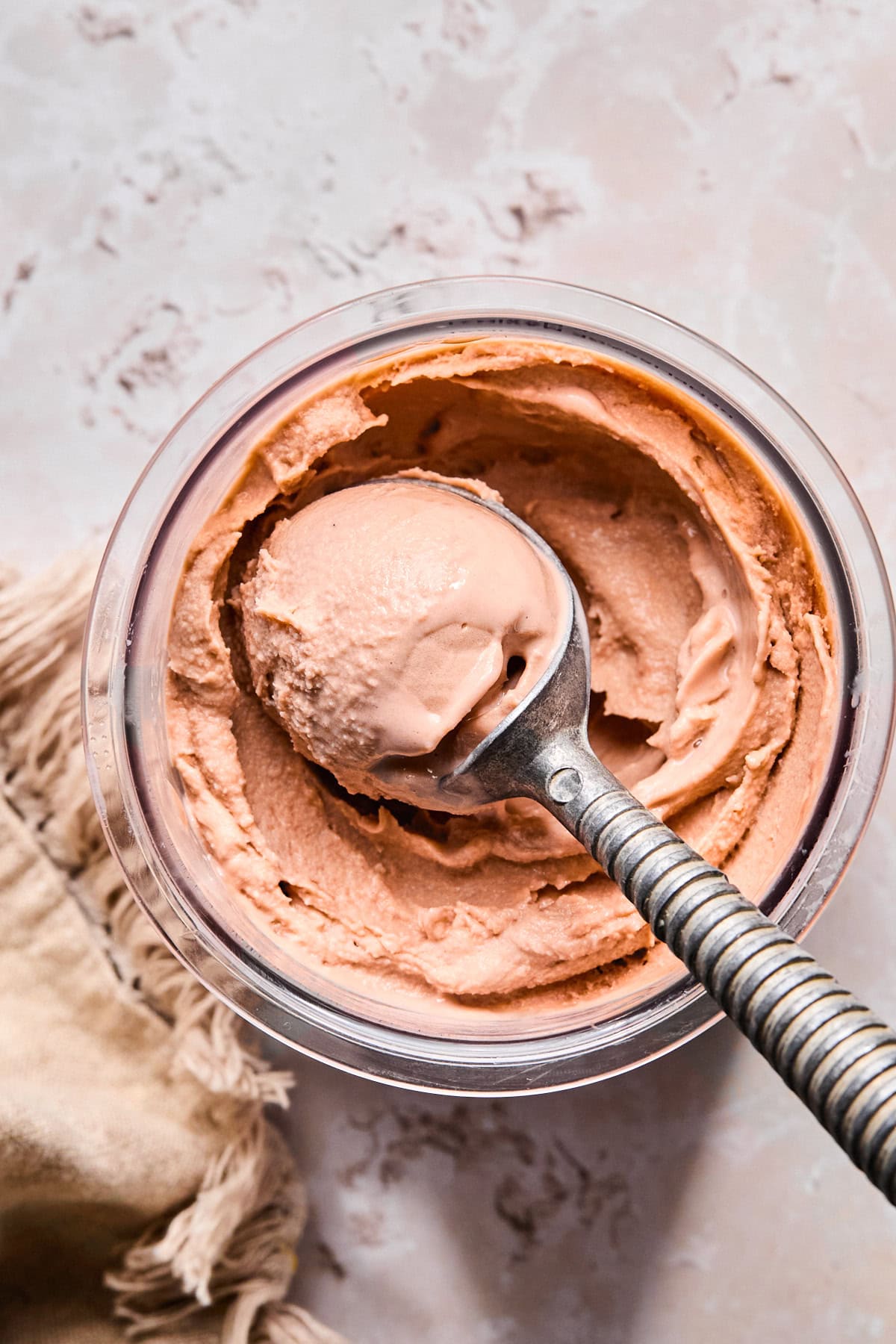 Ninja Creami pint container filled with chocolate ice cream while a silver ice cream scoop scoops out a serving.