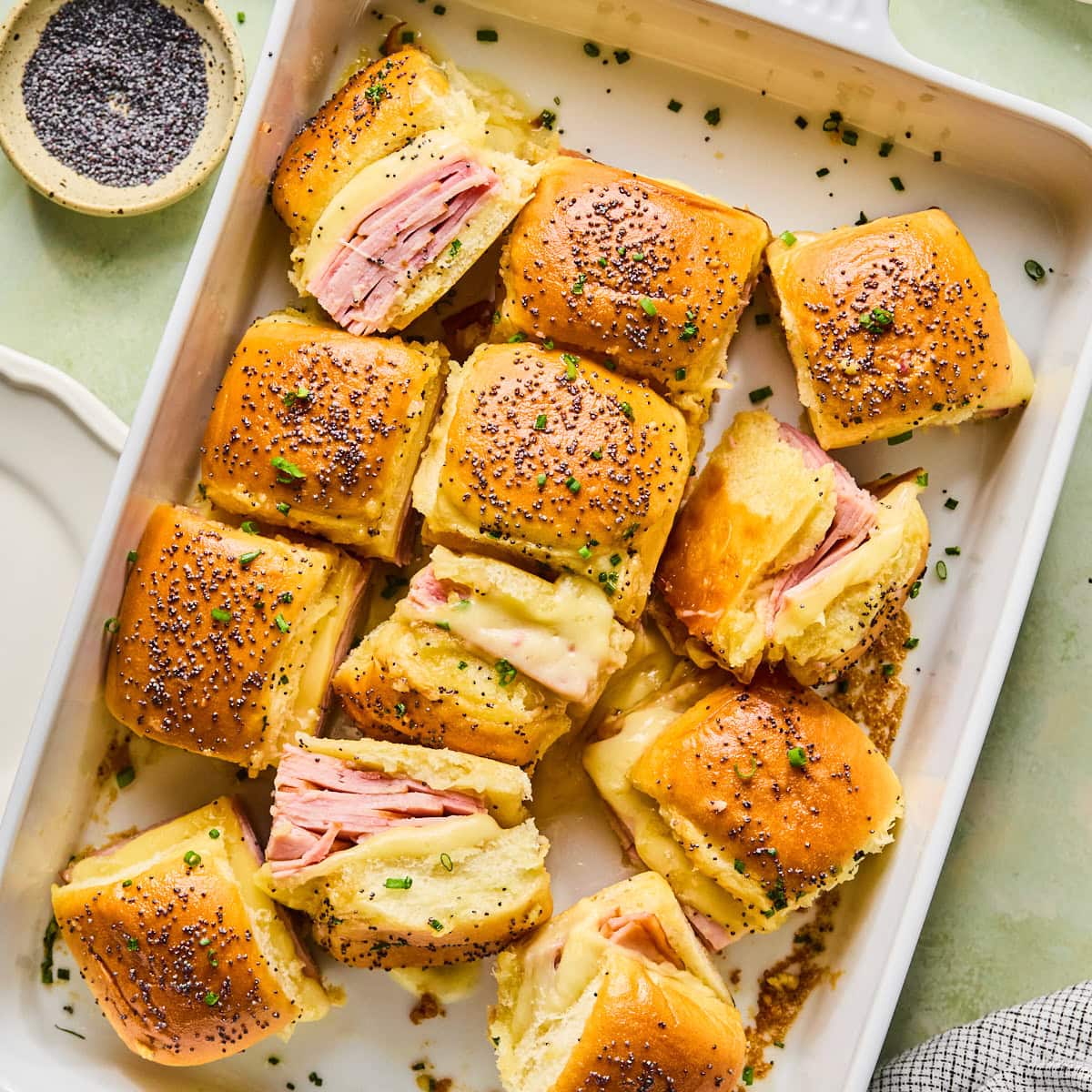 Hot ham and cheese sliders cut apart in a baking dish showing the melted cheese and ham inside.