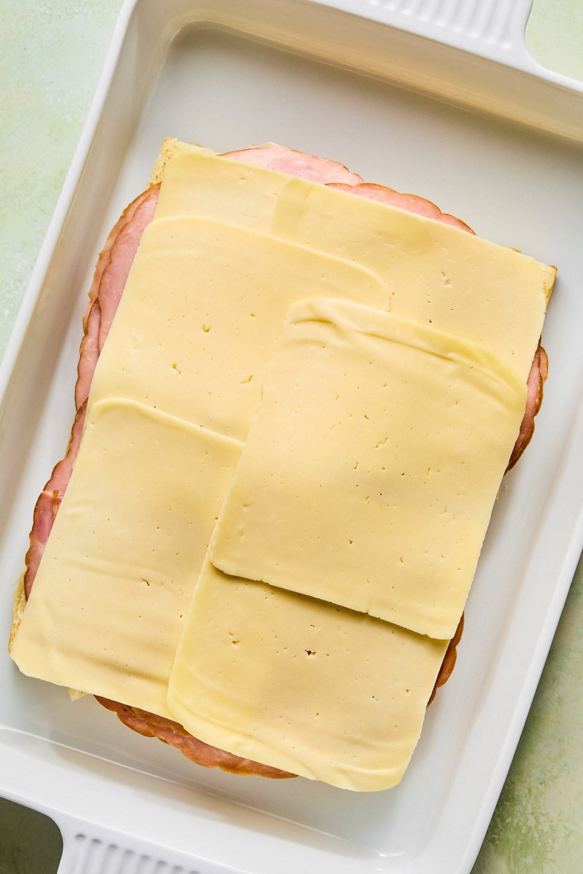 Layering sliced ham and cheese over the bottom half of Hawaiian rolls.