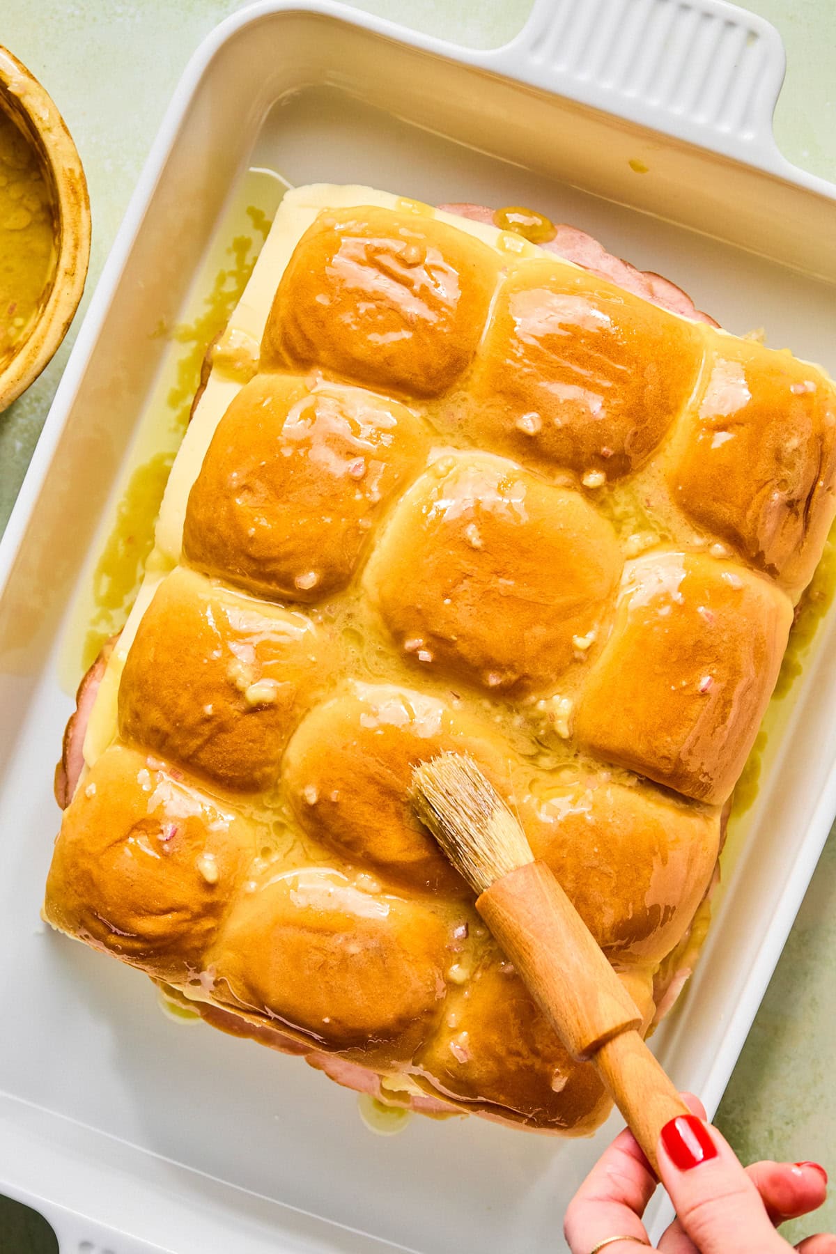 Brushing butter mixture over the tops of slider rolls before baking.