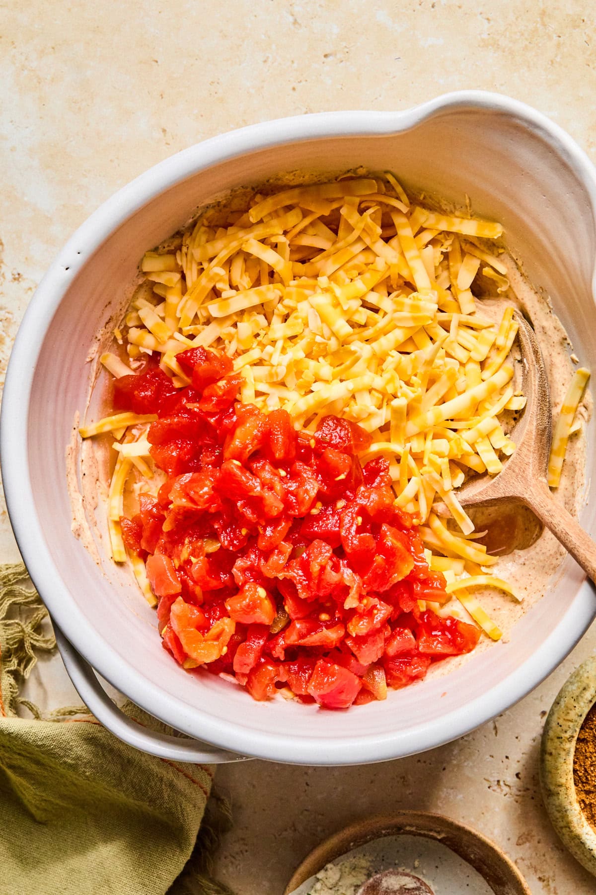 Shredded cheese and drained Rotel tomatoes being mixed into the seasoned sour cream mixture.