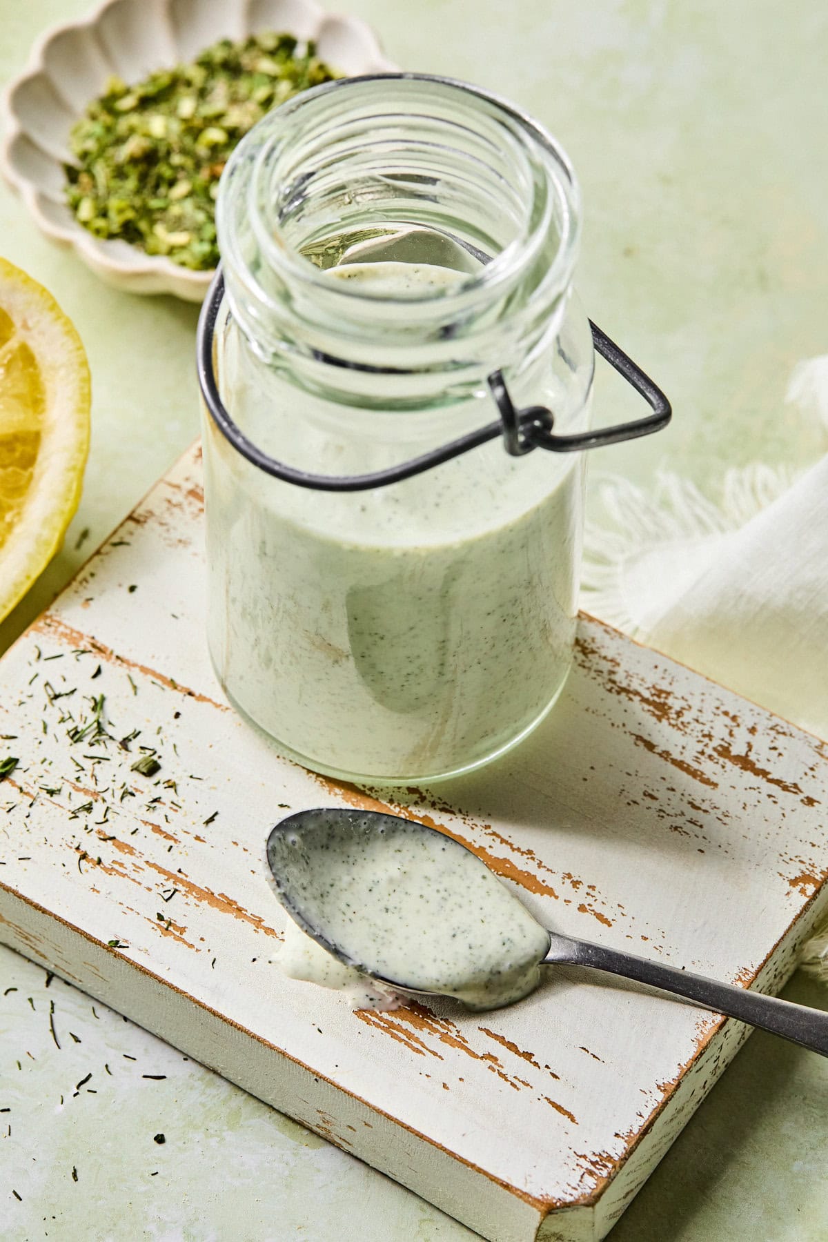 Jar of protein ranch dressing on a white rustic cutting board, with a spoon beside it coated in the dressing.